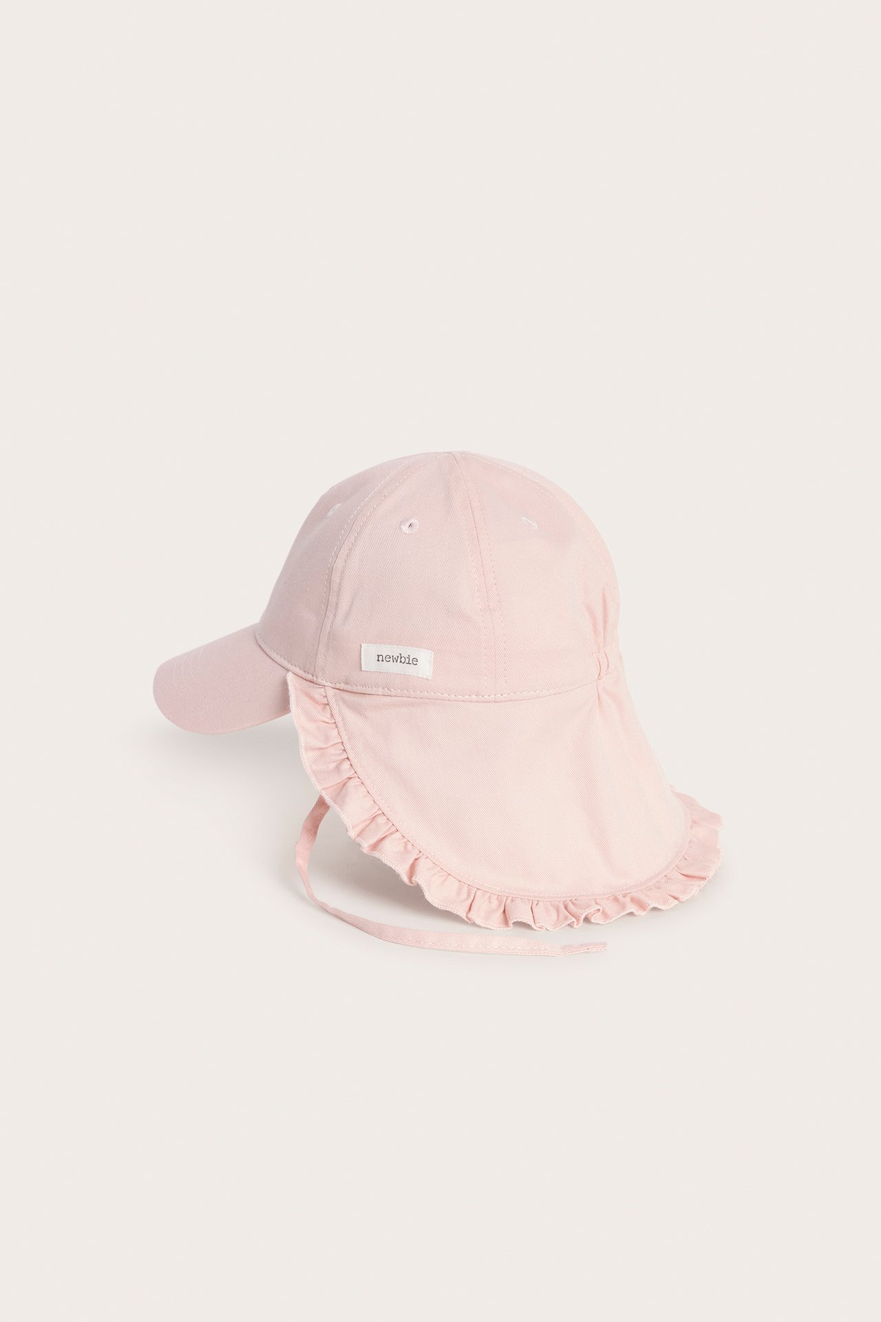 Sidevisning av en ensfarget rosa babycaps med volangkantet solbeskyttelse og knytebånd.