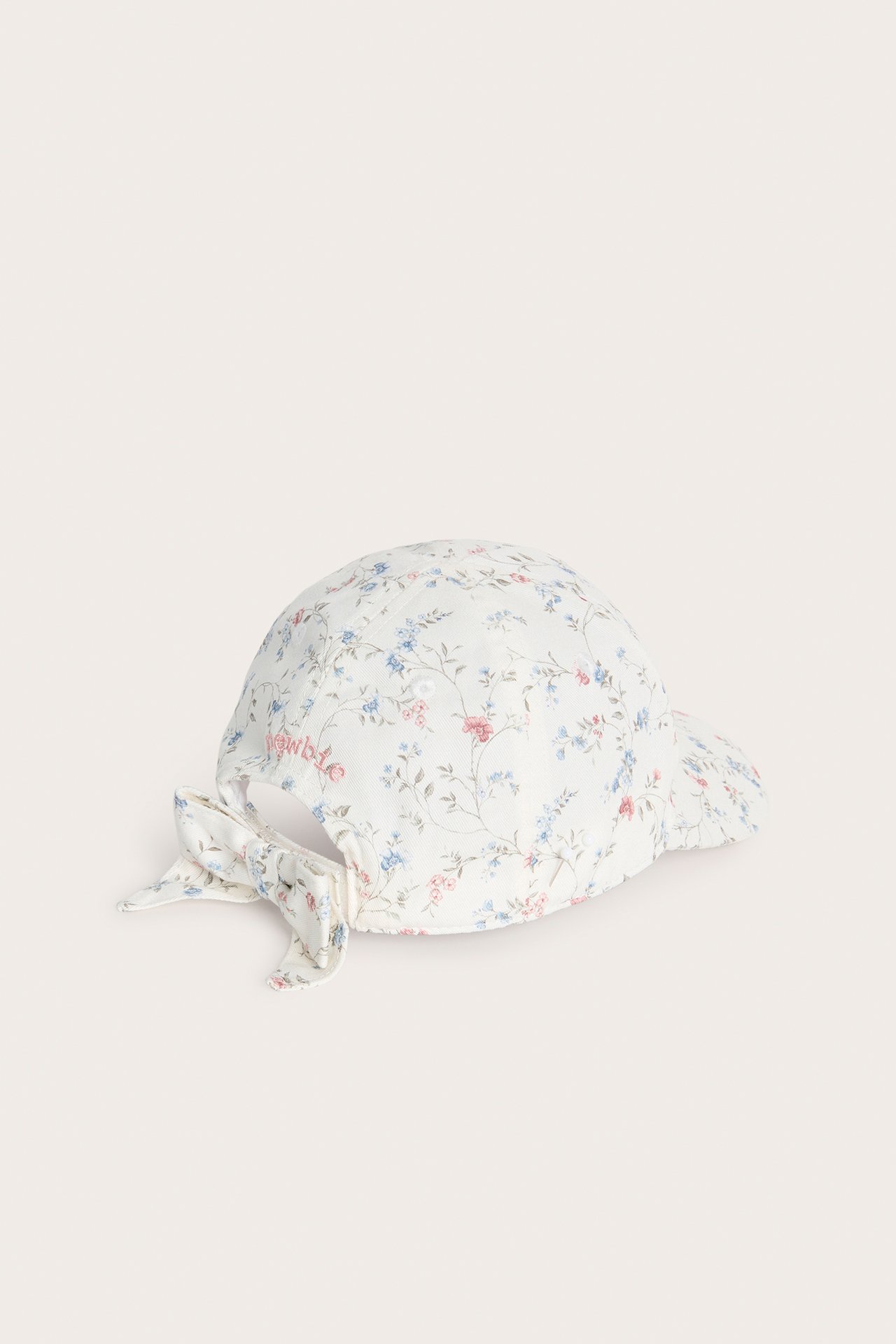 Side-bakfra-visning av en offwhite baby-/barnekeps med blomstermønster og dekorativ sløyfe bak.