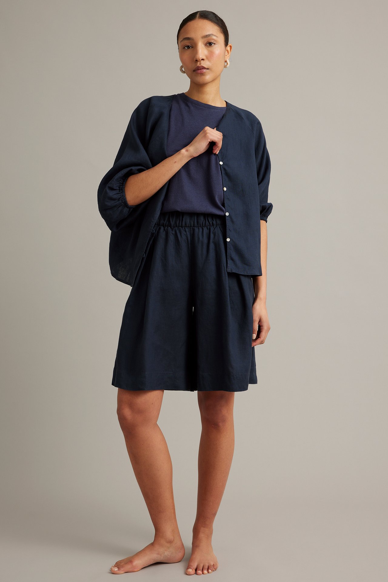 Naisen etukuva: Tummansiniset polvipituiset pellavashortsit, pellavaneule ja t-paita.