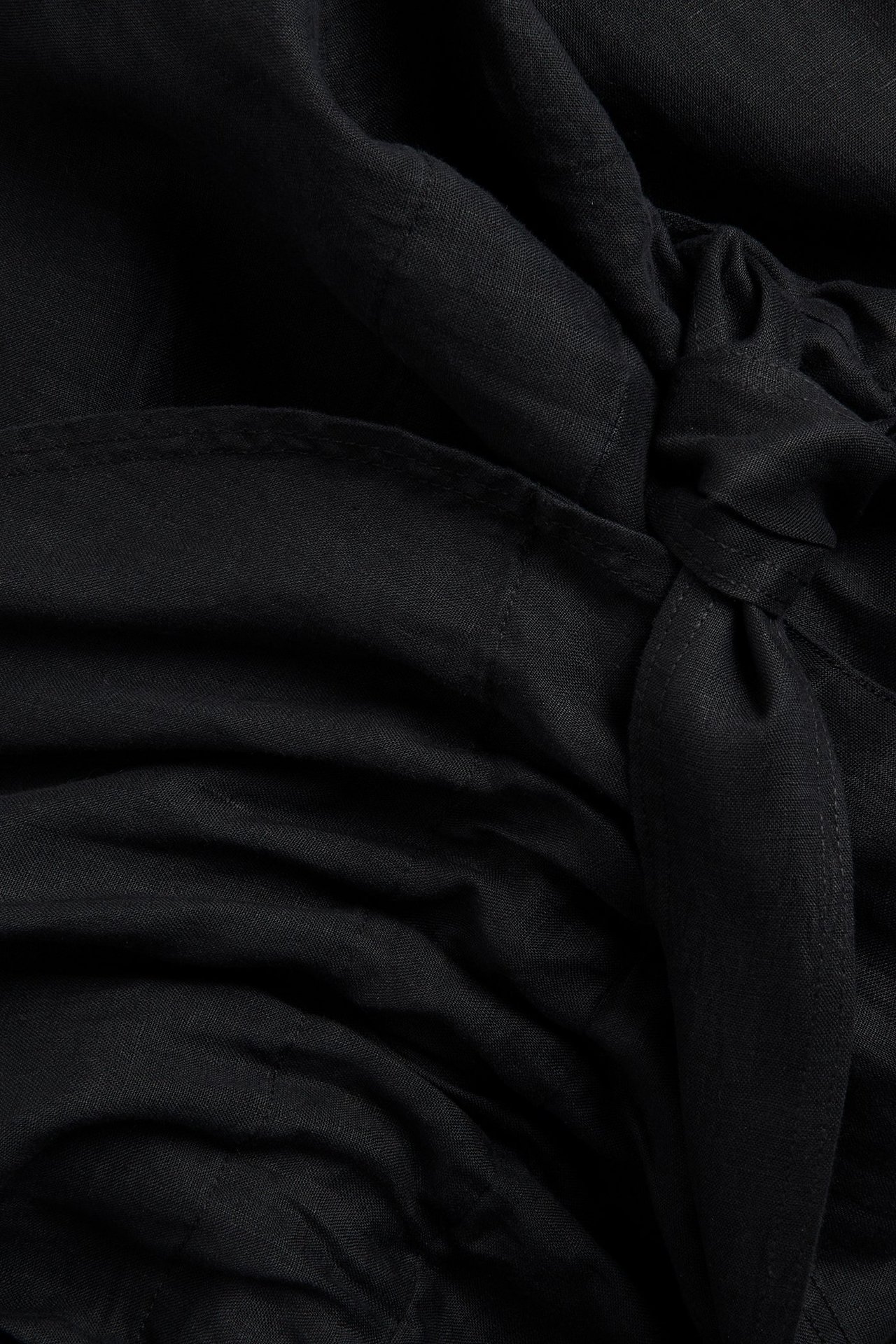 Zbliżenie czarnego lnianego kombinezonu z wiązaniem w elastycznej talii.