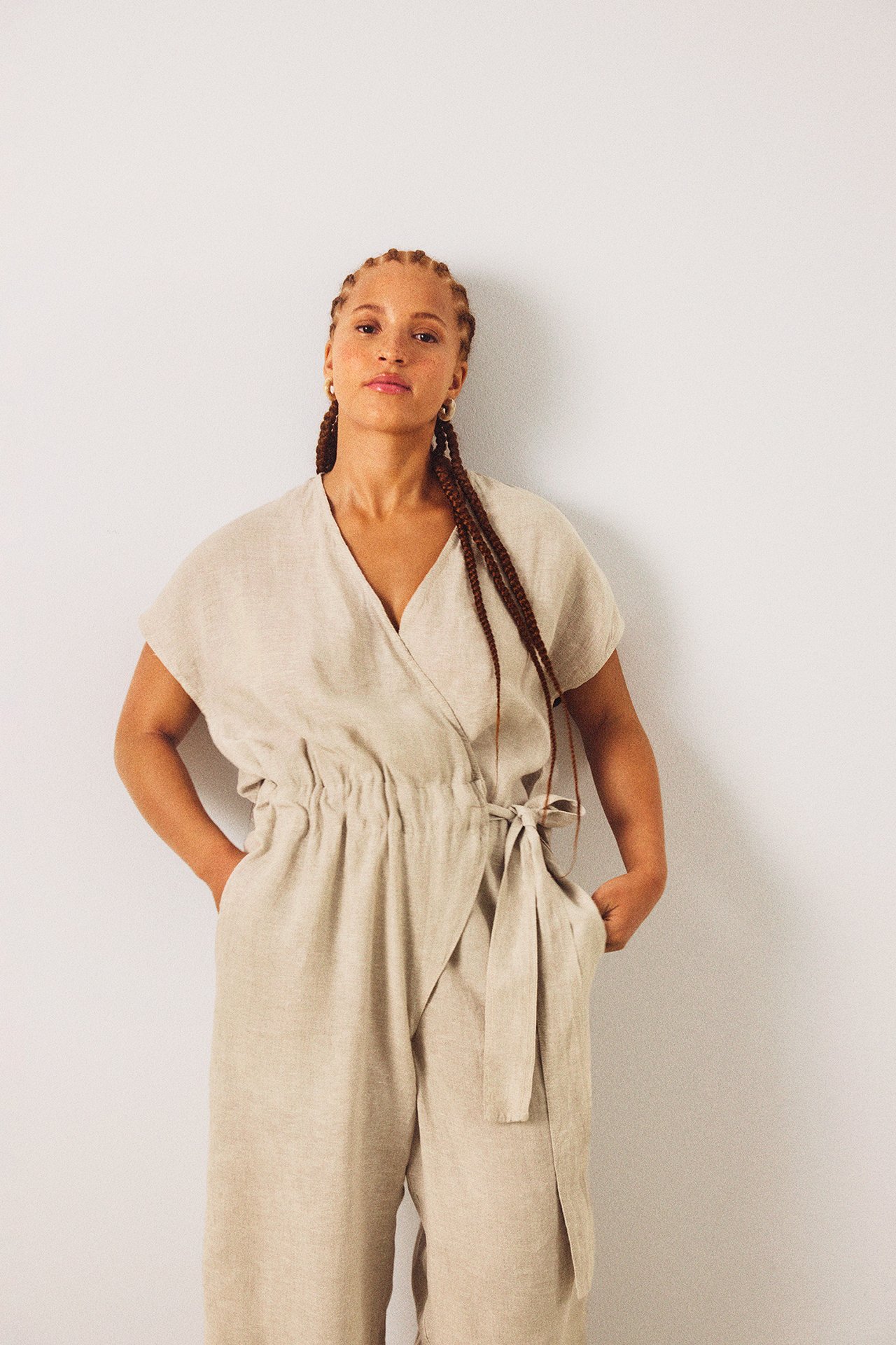 Frontvy av en kvinna som bär en beige jumpsuit i linne med omlottskuret liv och knytmidja.