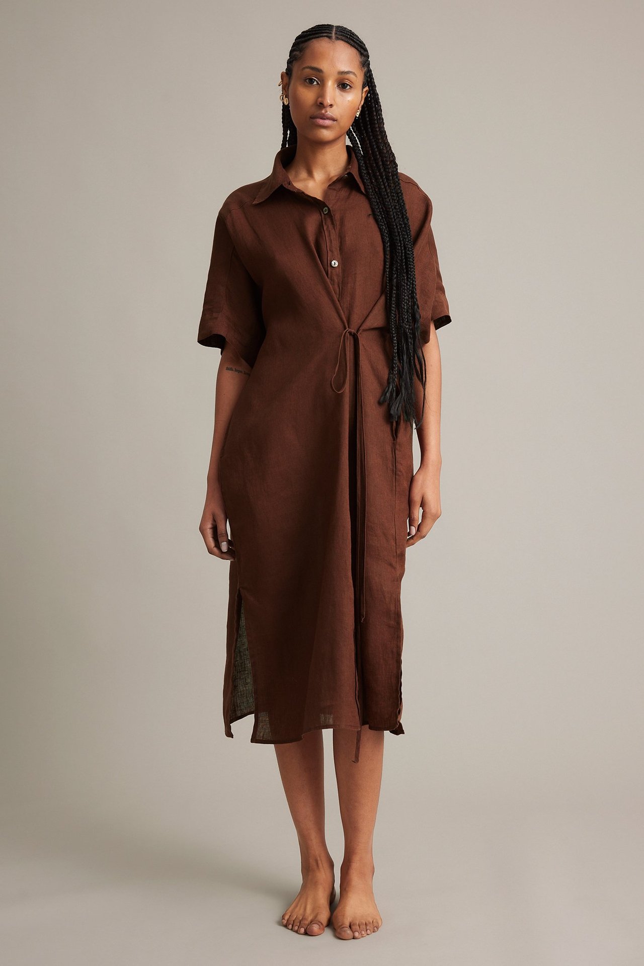 Edestä kuvattu nainen ruskeassa pellavapaitamekossa, jossa on kiristysnyöri vyötäröllä ja sivuhalkiot.