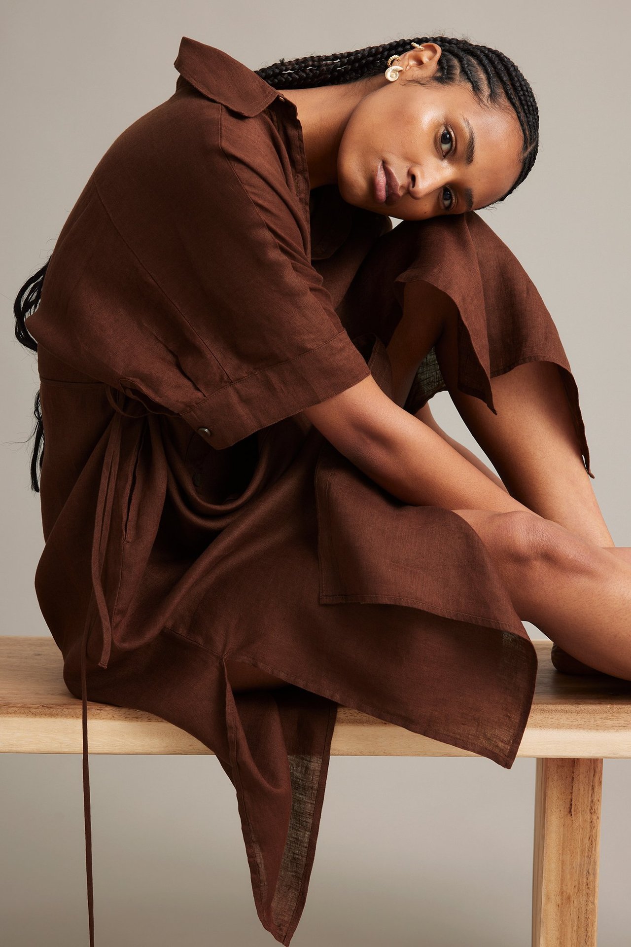 Sivukuva naisesta, jolla on ruskea pellavainen paitamekko kiristysnyörillä ja kultaiset korvakorut.