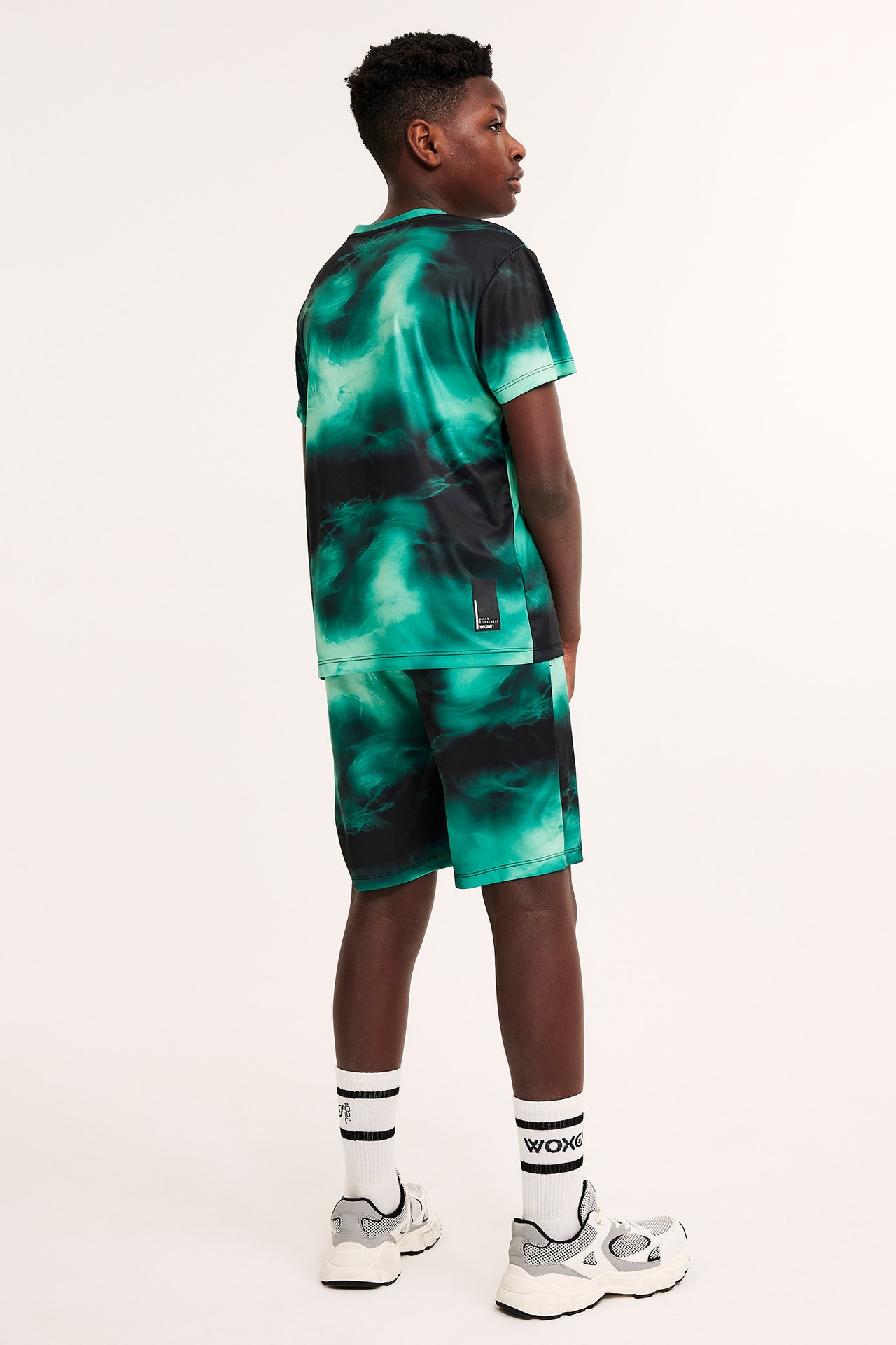 Bakifrån på ett barn i mörkgrönt mönstrat sportset i polyester, vita strumpor och grå sneakers.