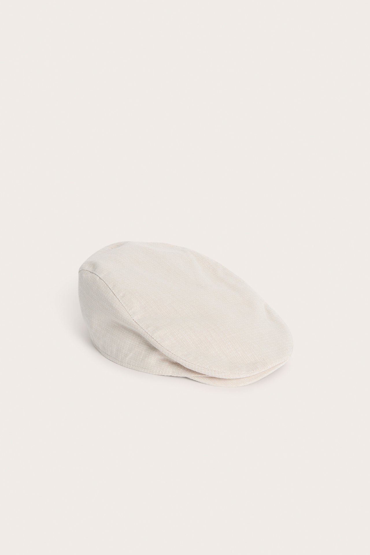 Sidovy av en enfärgad beige strukturvävd gubbkeps för barn.