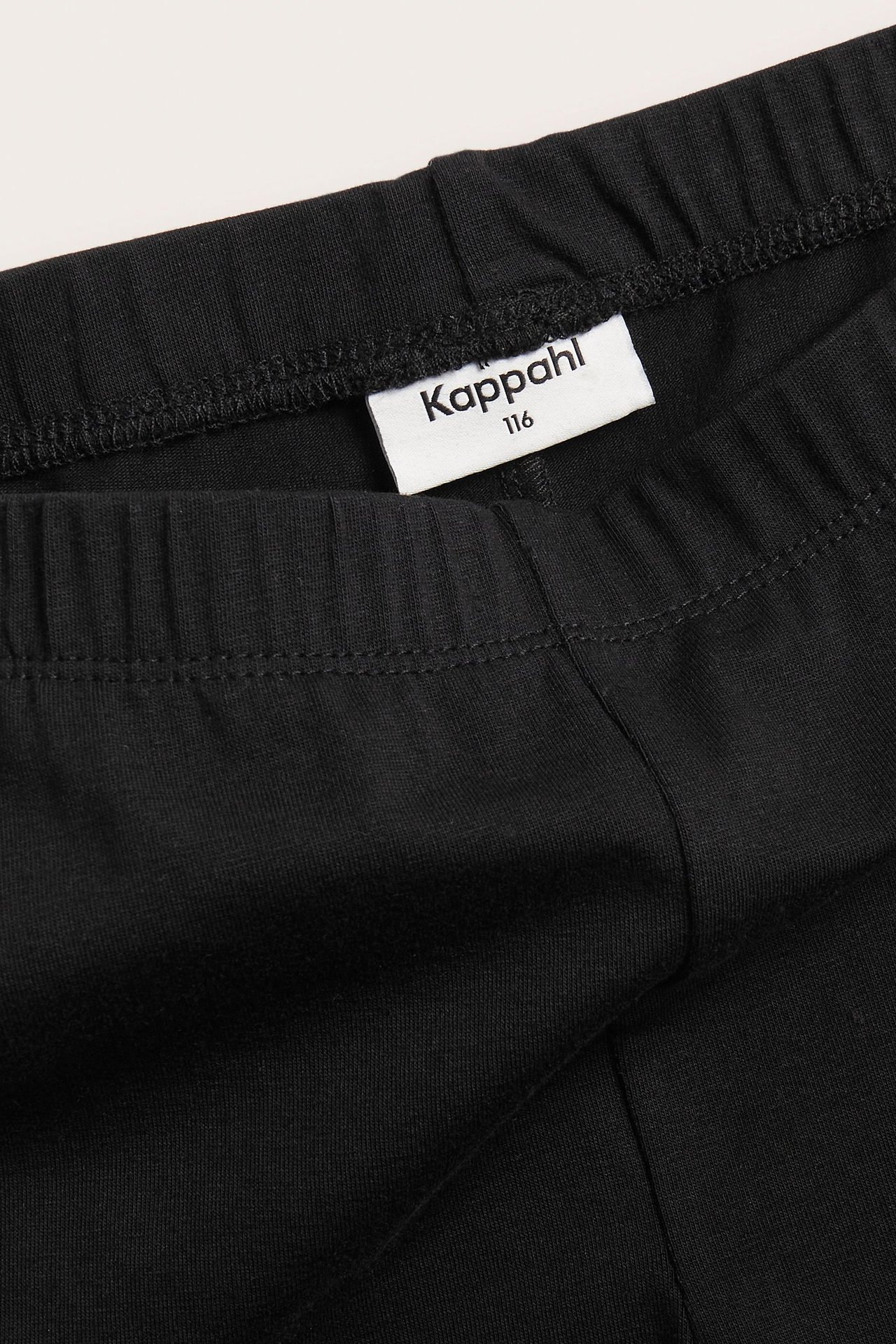 Zbliżenie na czarne legginsy 3/4 z elastycznym pasem i białą metką Kappahl.