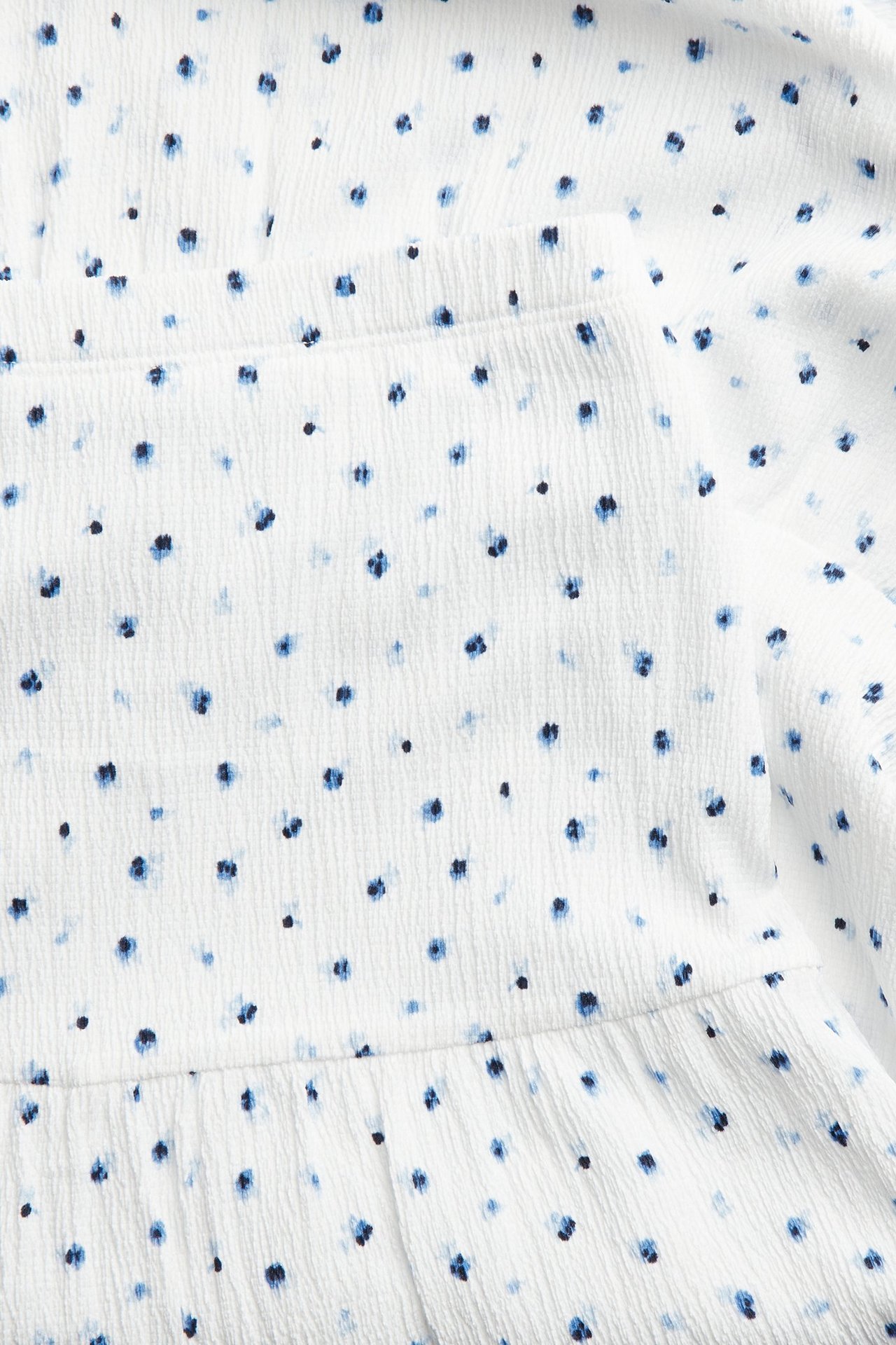 Zbliżenie białej, marszczonej spódnicy maxi z dżerseju w niebieski kwiatowy wzór.