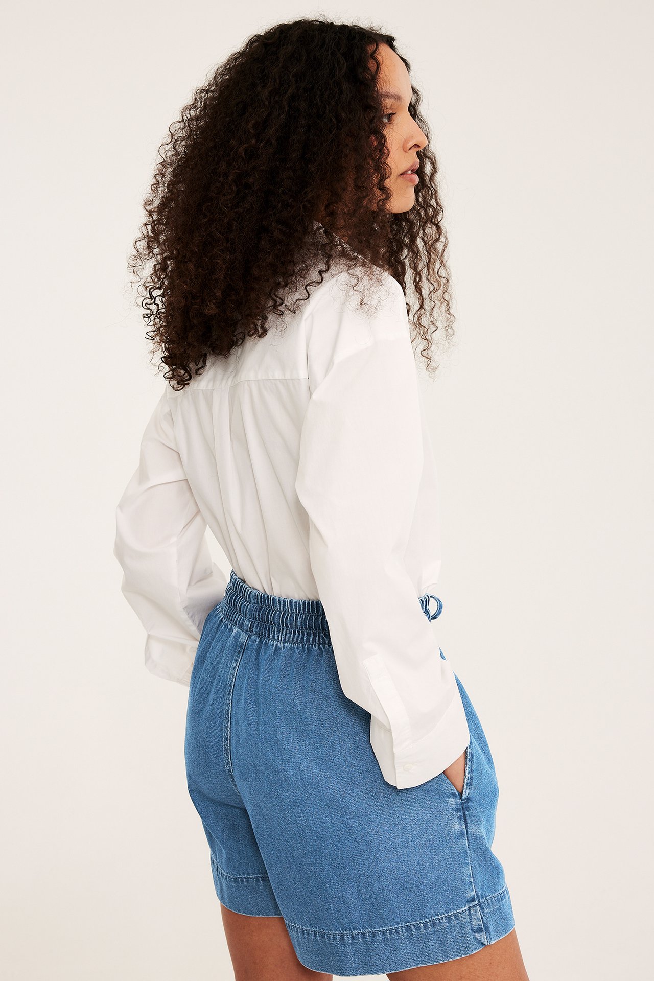 Kobieta z boku w niebieskich dżinsowych szortach pull-on z elastycznym pasem i białej koszuli.