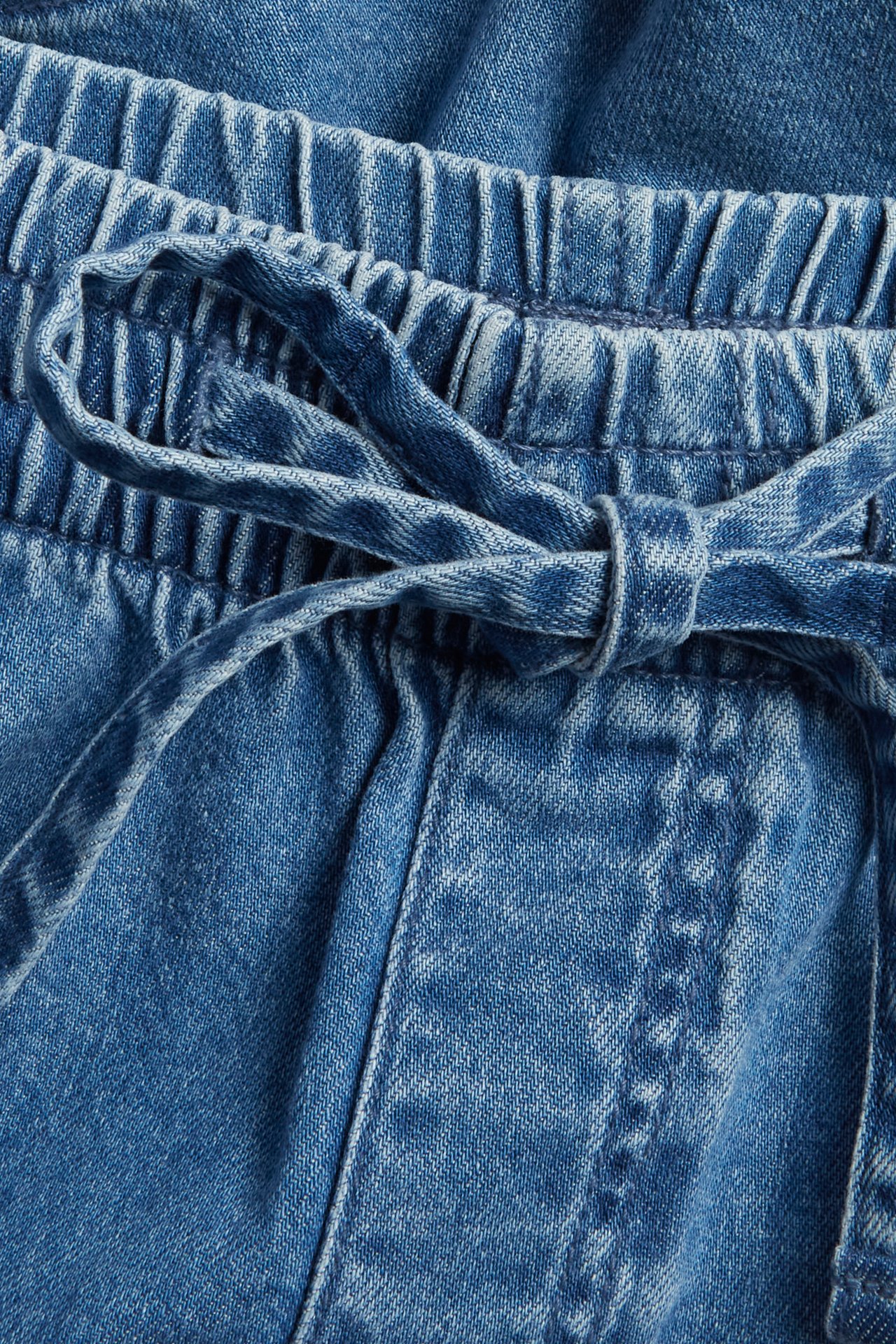 Zbliżenie na niebieskie szorty jeansowe typu pull-on z elastyczną talią i wiązanym sznurkiem.
