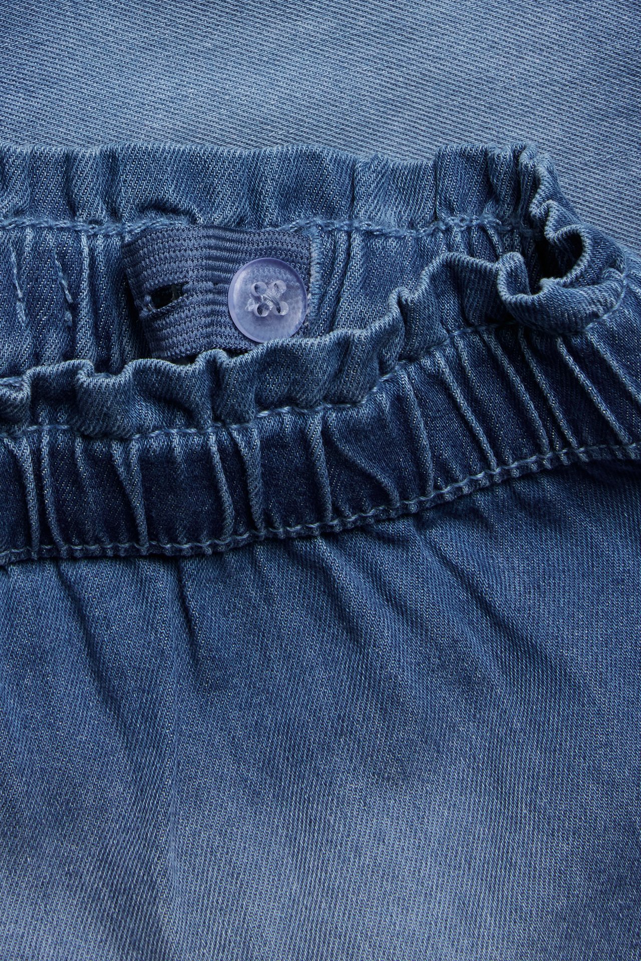 Närbild av ljusblåa mjuka jeansshorts för barn med resår i midjan och justerbar knapp.