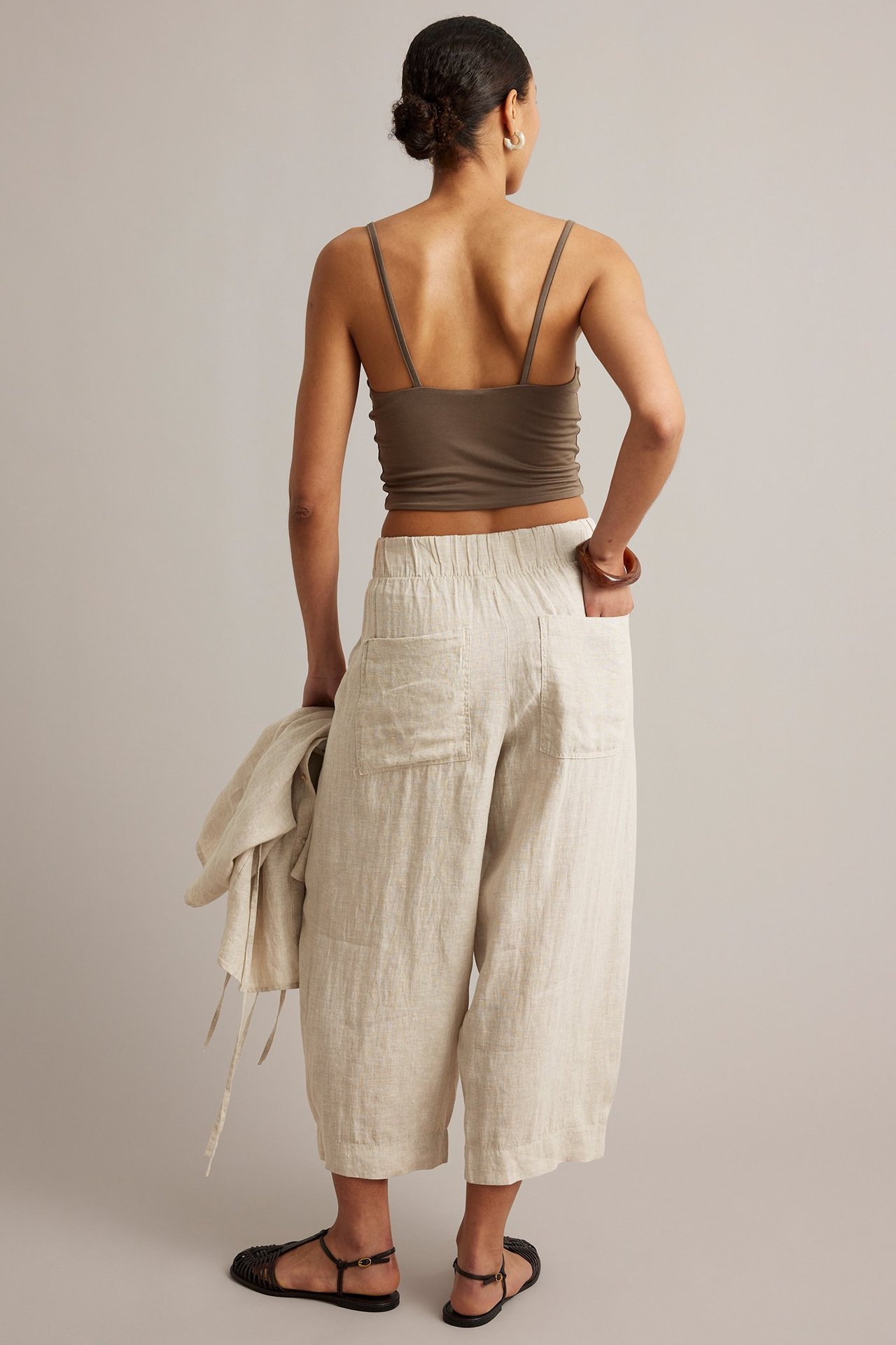 Bakfra: kvinne i beige melert linbukse med barrel fit, brun topp, holder en linjakke.