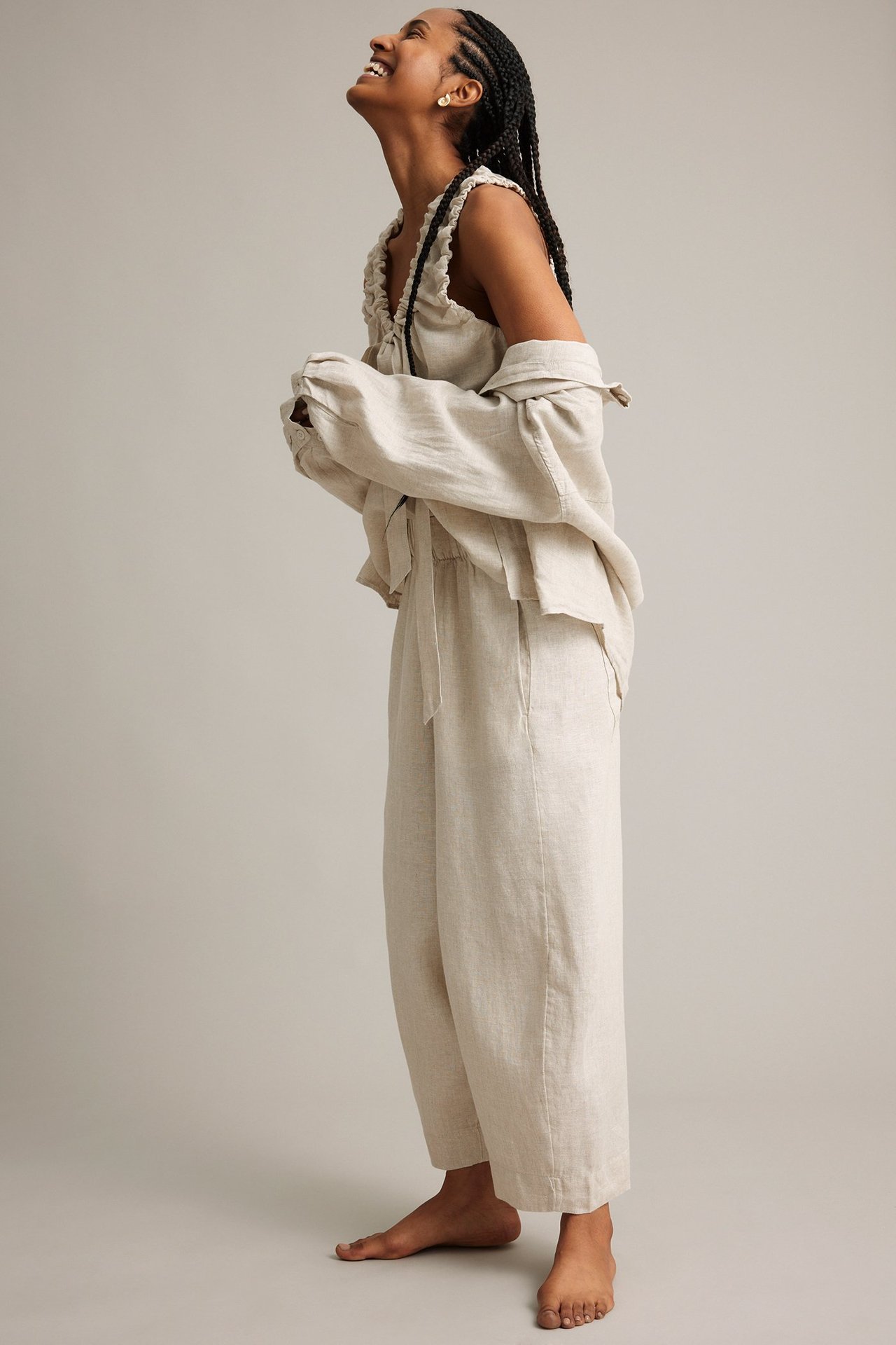 Sidebilde av kvinne i beige melert linbukse med barrel leg, en volangtopp og en åpen skjorte.