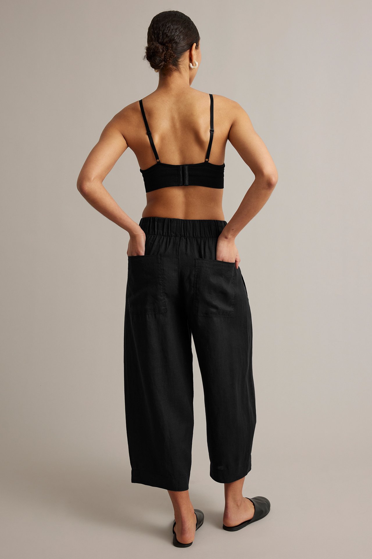 Kvinne bakfra i svarte barrel-leg linbukser, svart BH og svarte slip-on sandaler.