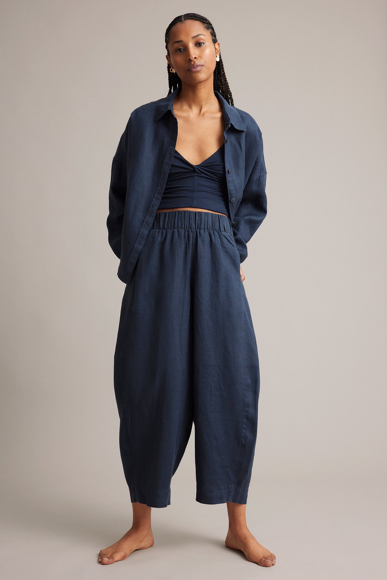 Framifrån: Kvinna i mörkblå linnebyxor med barrel leg, matchande öppen skjorta och crop top.