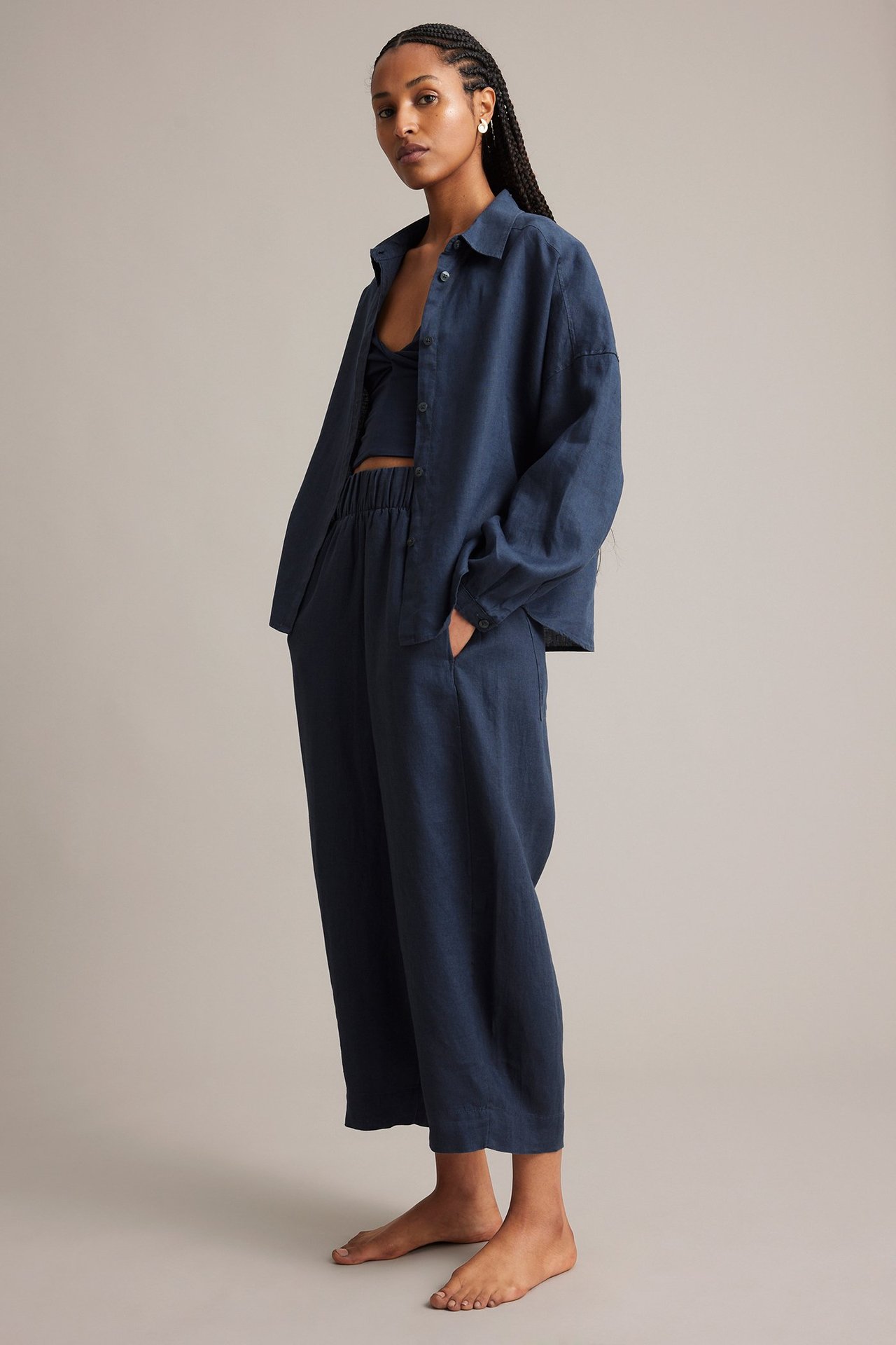 Sida: kvinna i mörkblå linnebyxor med barrel leg, matchande öppen skjorta och crop top.