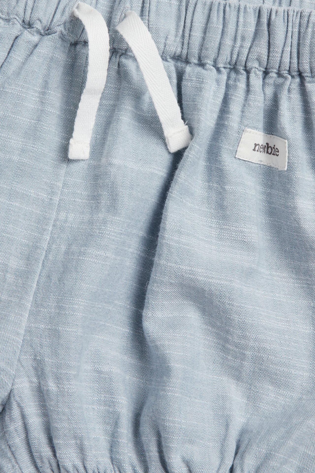 Lähikuva sinisistä chambray-shortseista, joissa joustava vyötärö ja valkoinen kiristysnyöri.