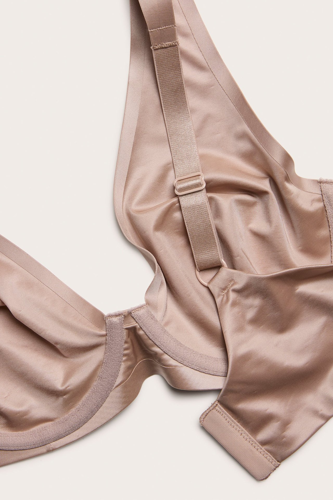 Zbliżenie na jasnoróżowy biustonosz z fiszbinami z gładkiej satynowej mikrofibry z regulowanymi ramiączkami.