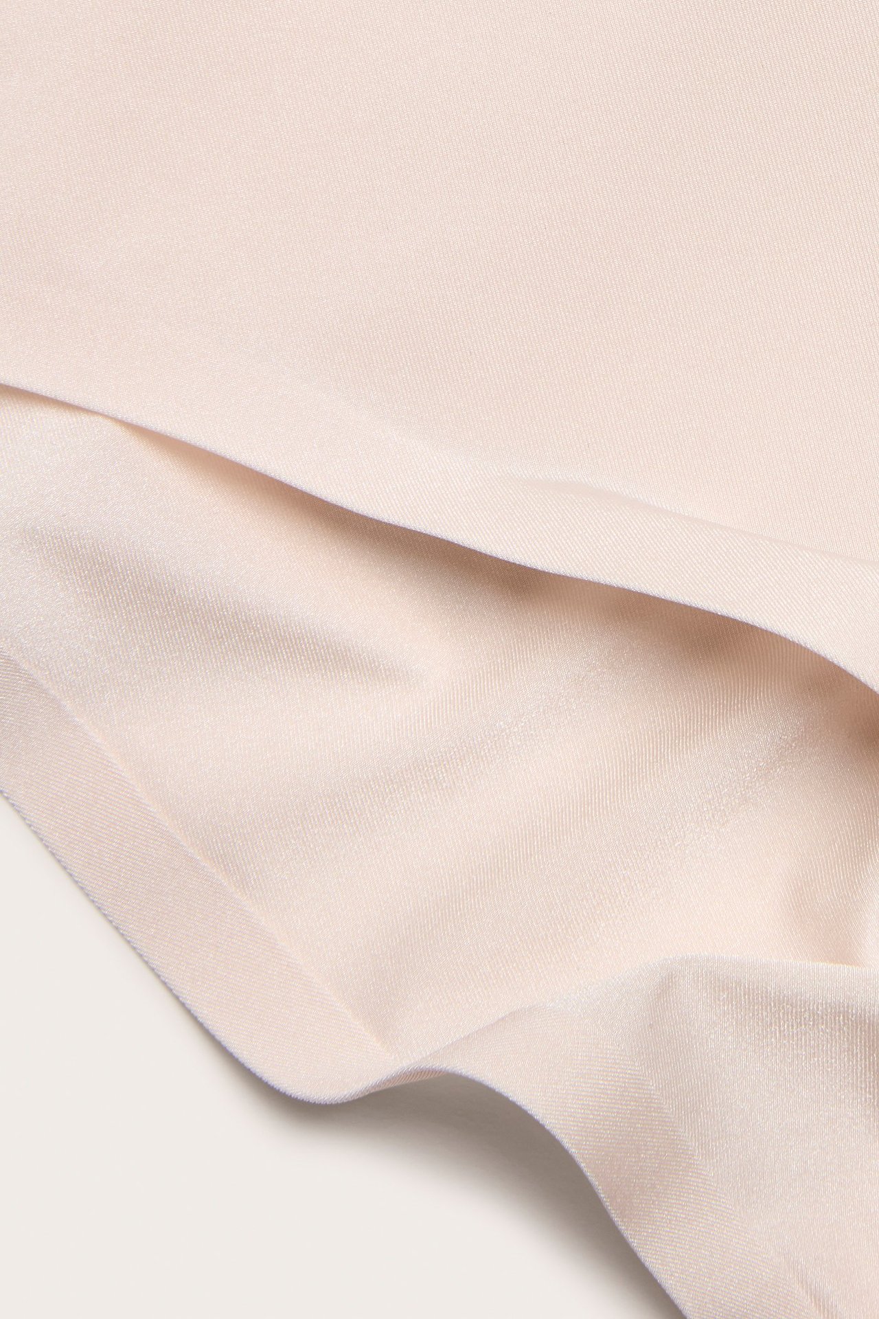 Zbliżenie beżowych majtek z elastycznej mikrofibry z połyskiem i klejonymi krawędziami.