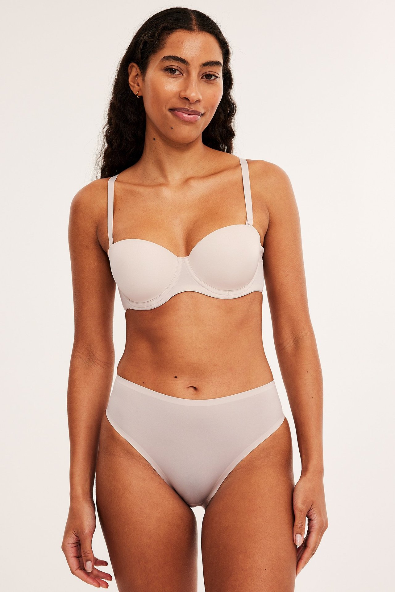 Frontbilde av en kvinne i beige mid-rise truser med limte kanter og en matchende beige stroppeløs BH.