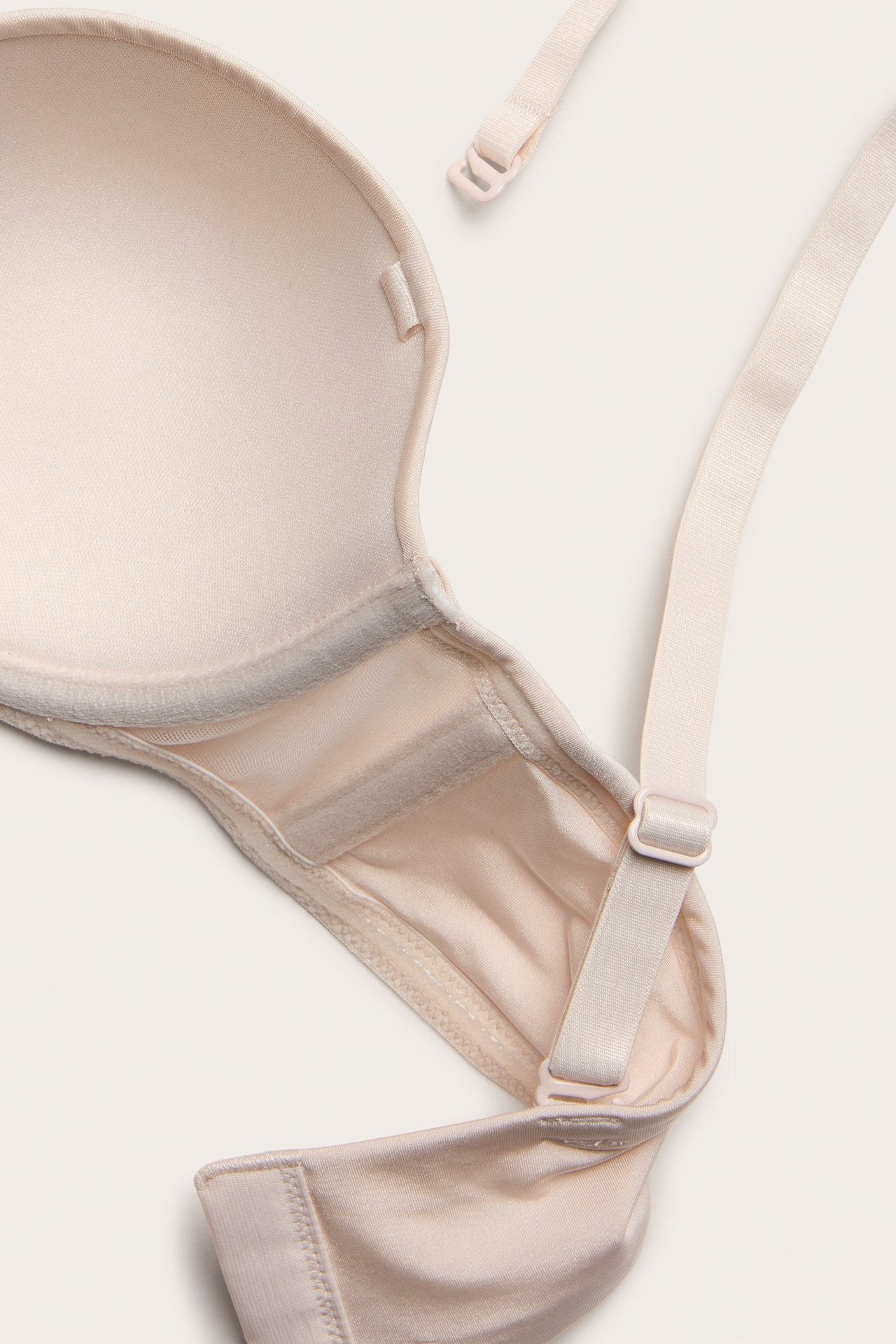 Zbliżenie beżowego, usztywnianego biustonosza typu balconette z widocznym odpiętym regulowanym ramiączkiem.