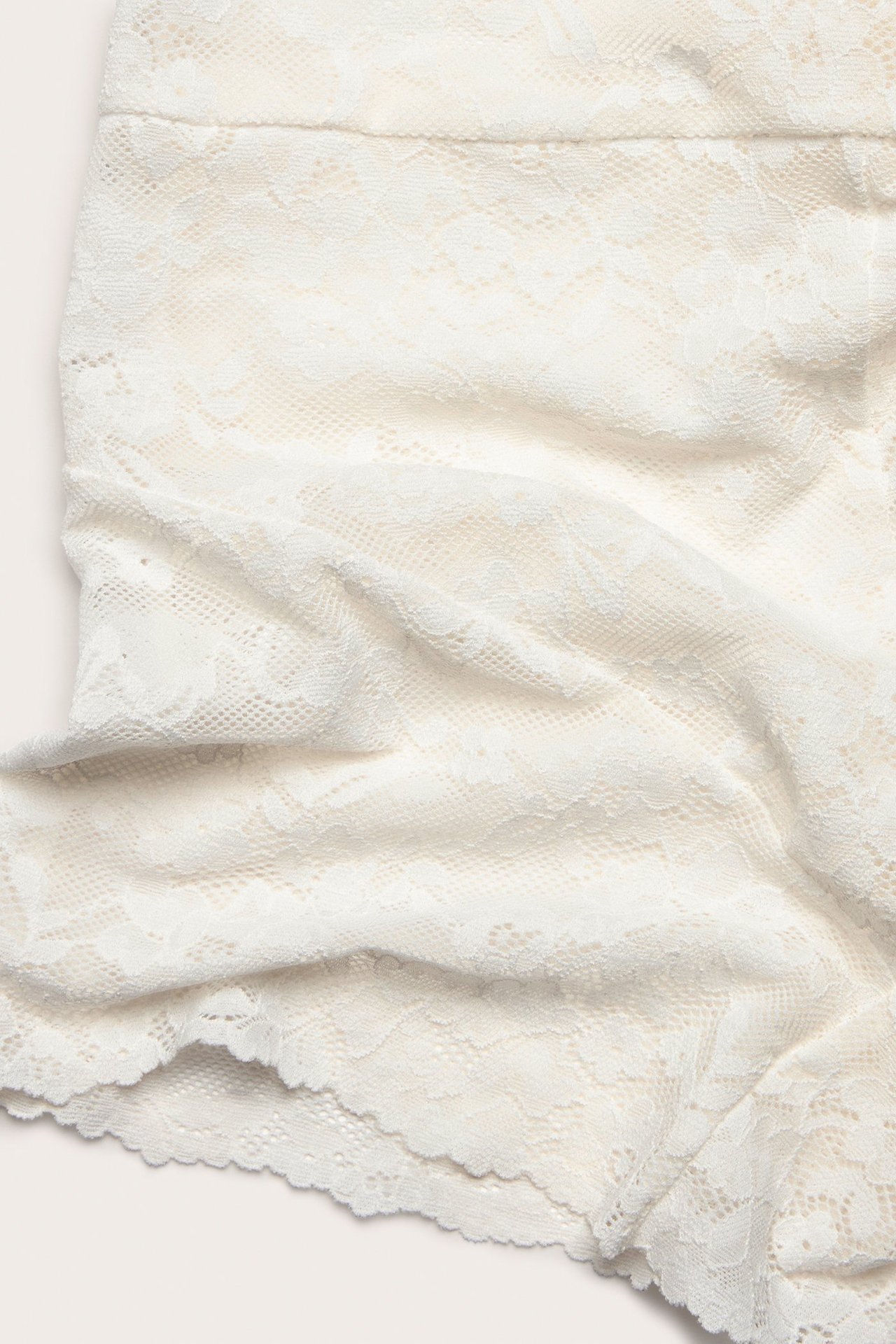 Zbliżenie na ecru koronkowe szorty, ukazujące delikatny kwiatowy wzór.