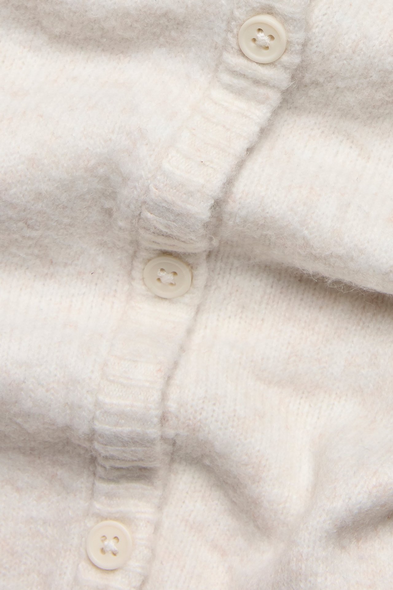 Zbliżenie białego, krótkiego kardiganu z jasnymi guzikami z przodu.