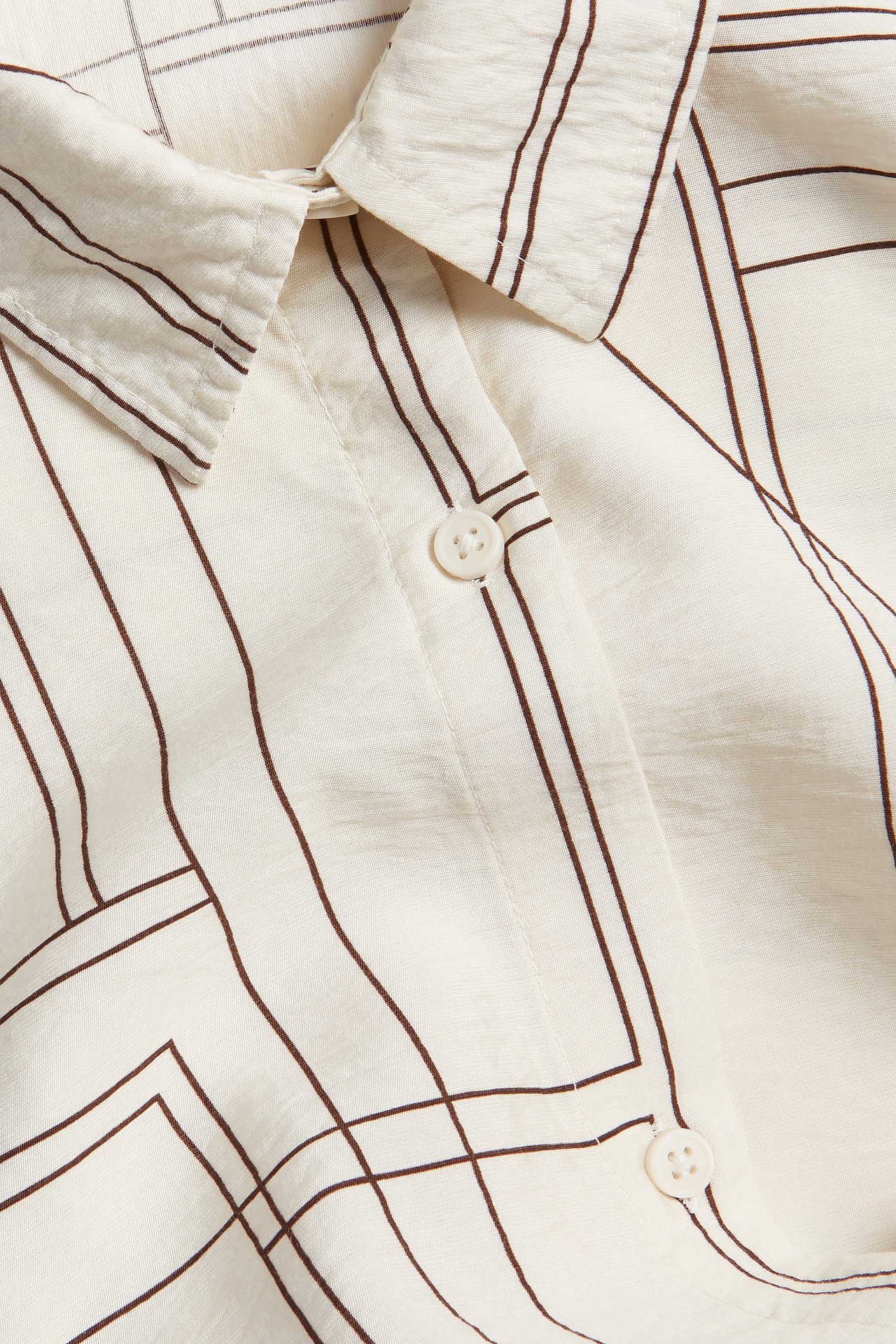Närbild av en offwhite skjortklänning i viskos med mörka geometriska linjer, krage och vita knappar.