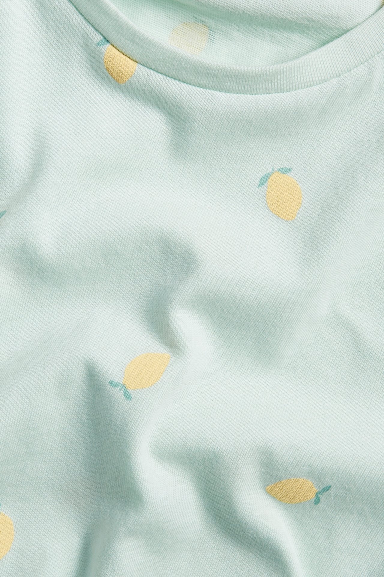 Närbild på en ljusgrön T-shirt i bomull för barn med gult citronmönster.