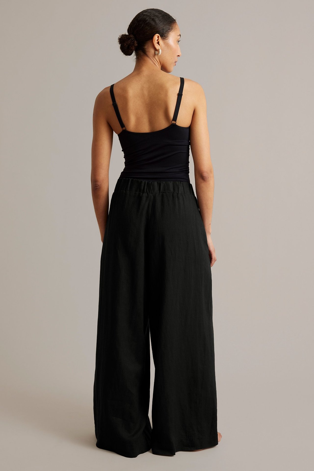 Nainen selin mustissa leveälahkeisissa pellavahousuissa joustavalla vyötäröllä ja mustassa topissa.