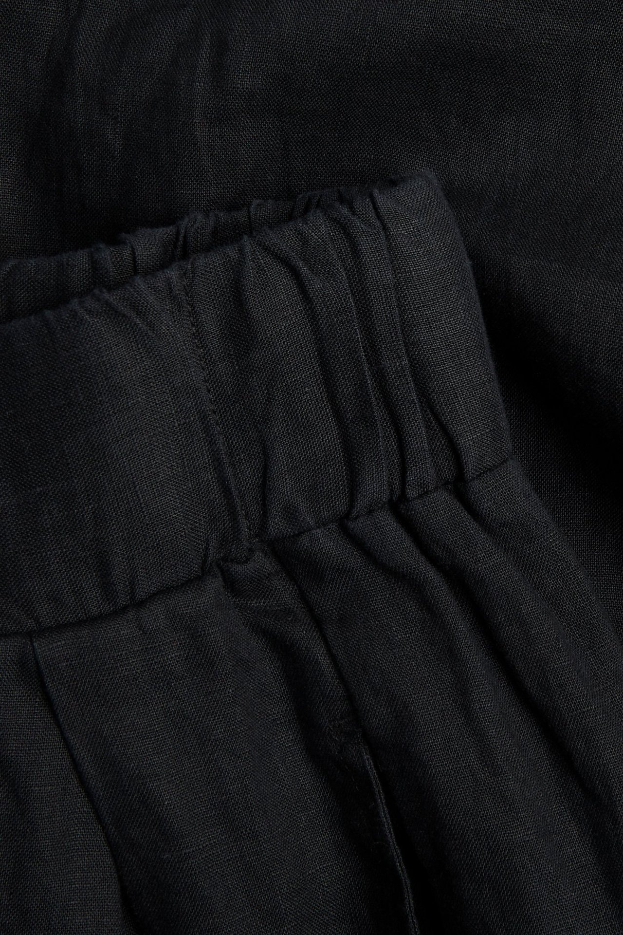 Zbliżenie czarnych lnianych spodni z szerokimi nogawkami, ukazujące elastyczny pas i teksturę tkaniny.