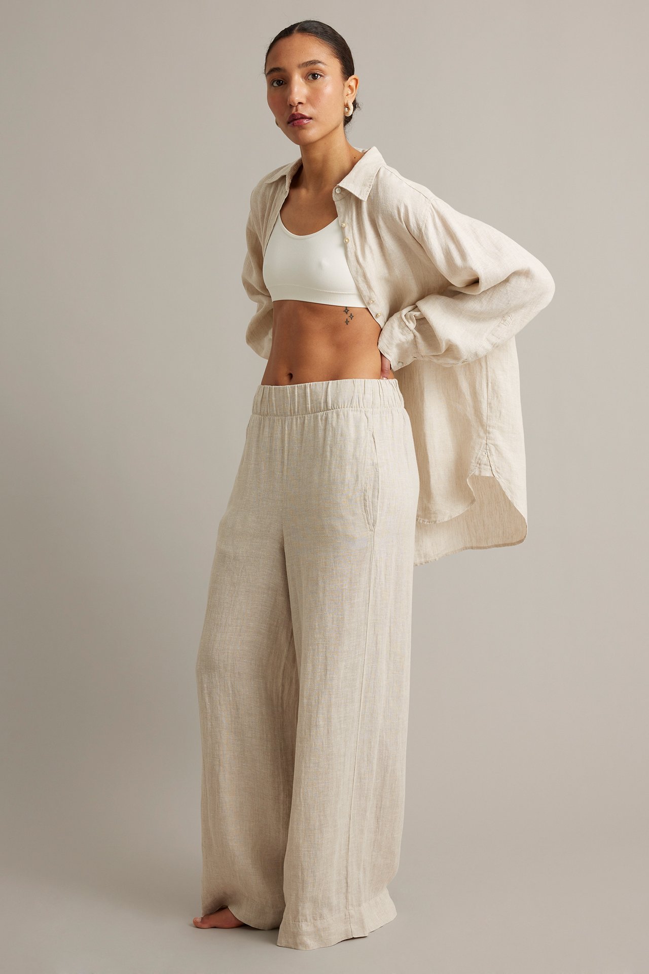 Frontutsikt: Kvinne i beige melert linbukse med vide ben, hvit crop top og åpen beige linskjorte.