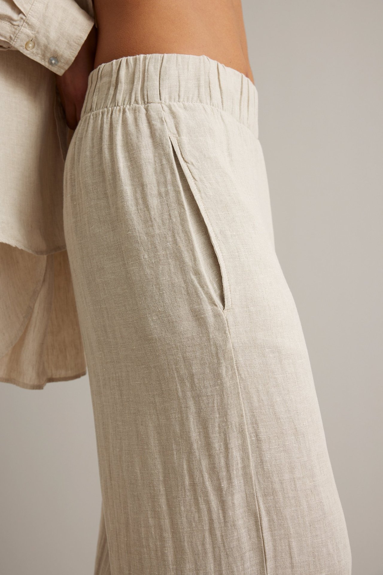 Sidebilde: Kvinne i beige melert linbukse med vide ben, strikk i midjen og sidelomme. Matchende linskjorte.