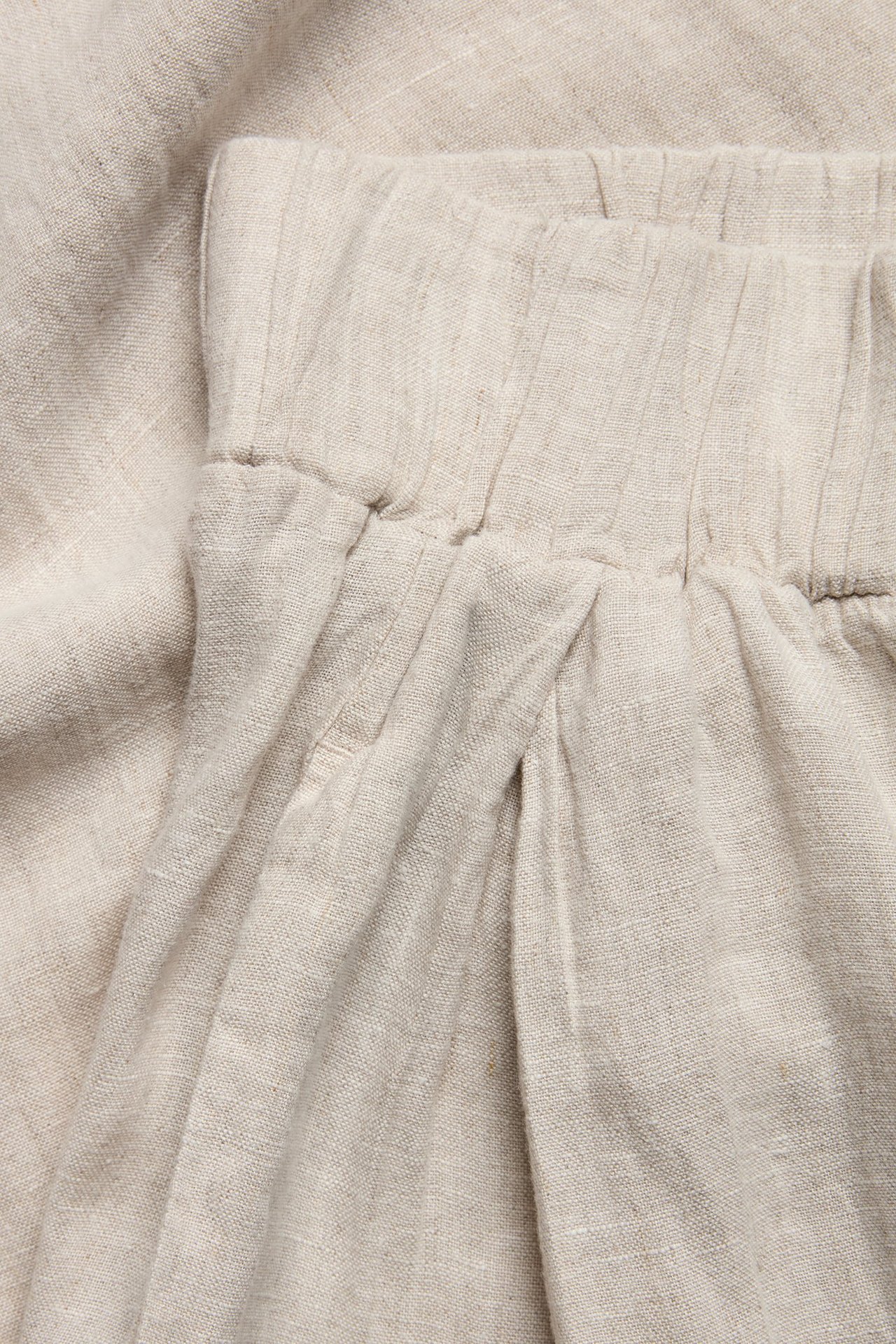 Zbliżenie beżowych melanżowych lnianych spodni z elastyczną talią i zakładkami.