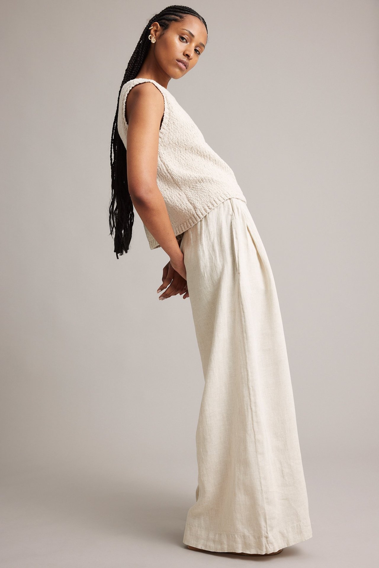 Sivukuva naisesta beigenvärisissä meleeratuissa leveälahkeisissa pellavahousuissa ja vaaleanbeigessä neulepaidassa.