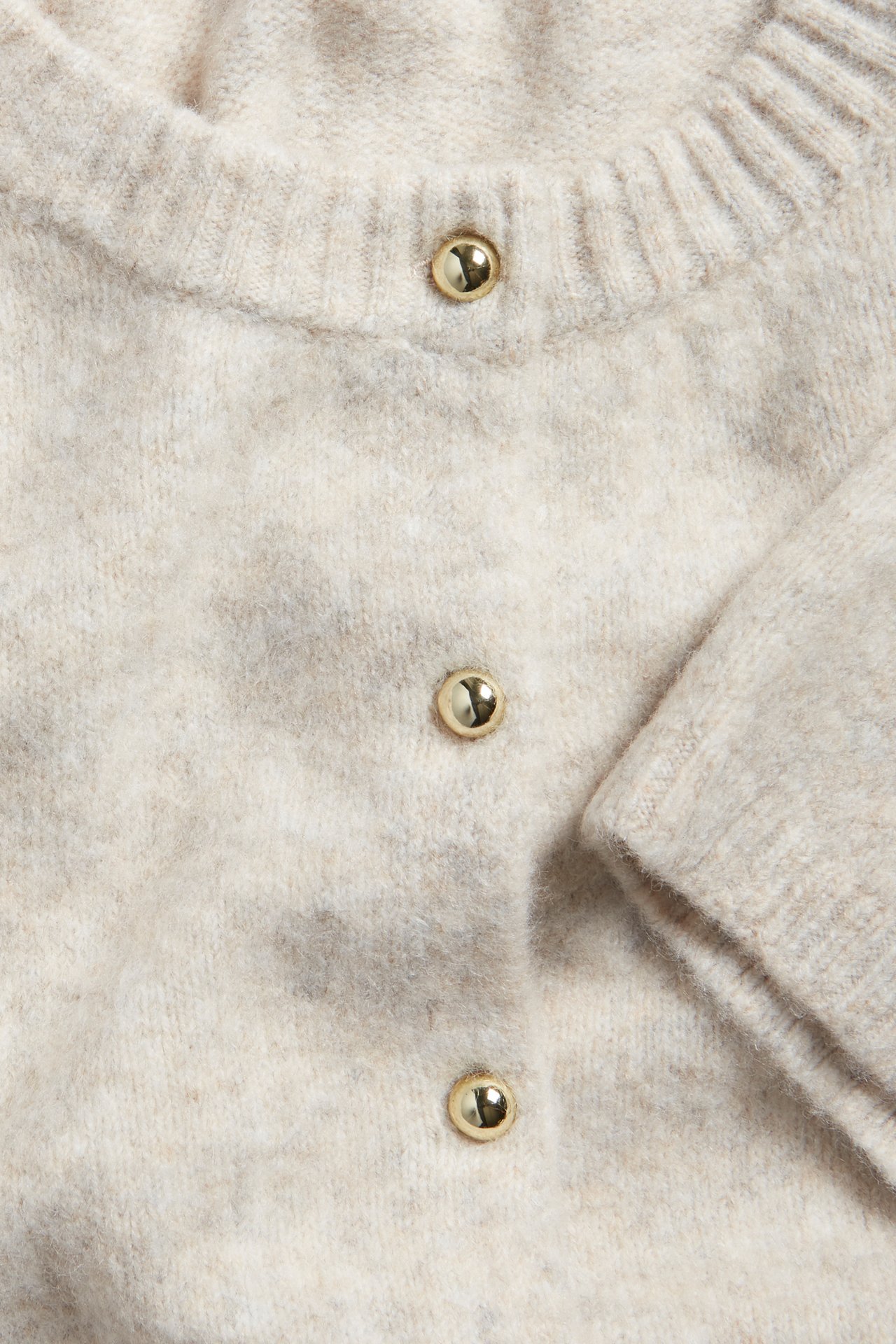 Nærbilde av en beige melert kortermet cardigan med gullfargede knapper på knappestolpen.