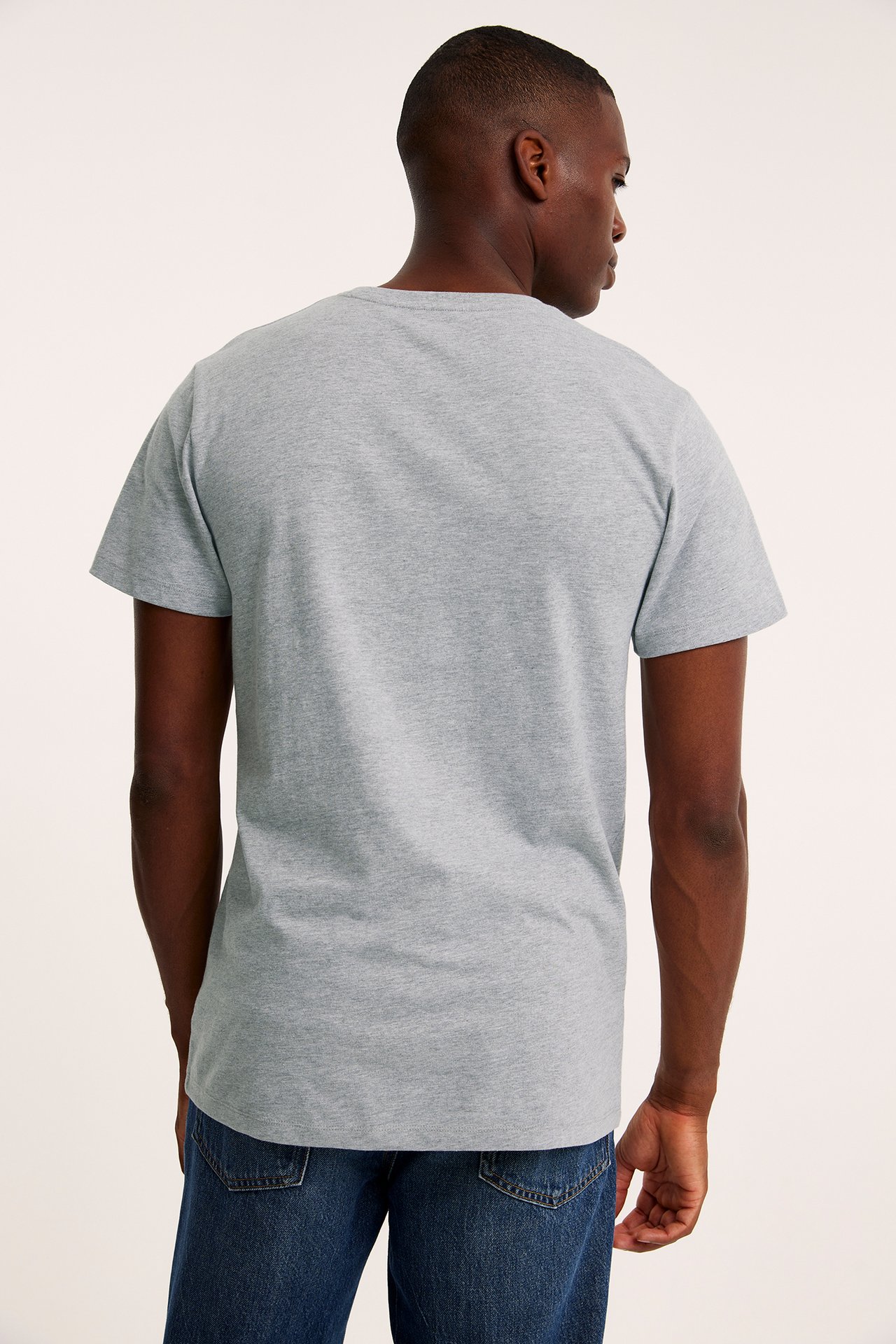 Ryggvy av en man i en gråmelerad kortärmad t-shirt med rund hals och blå jeans.