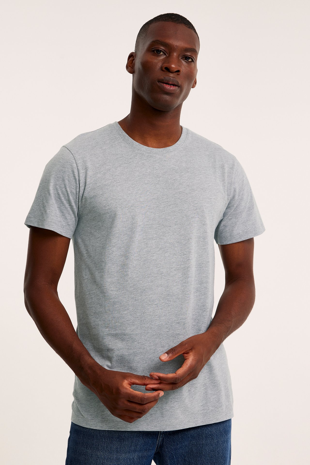 Mężczyzna z przodu w szarym melanżowym T-shircie z okrągłym dekoltem i niebieskich dżinsach.