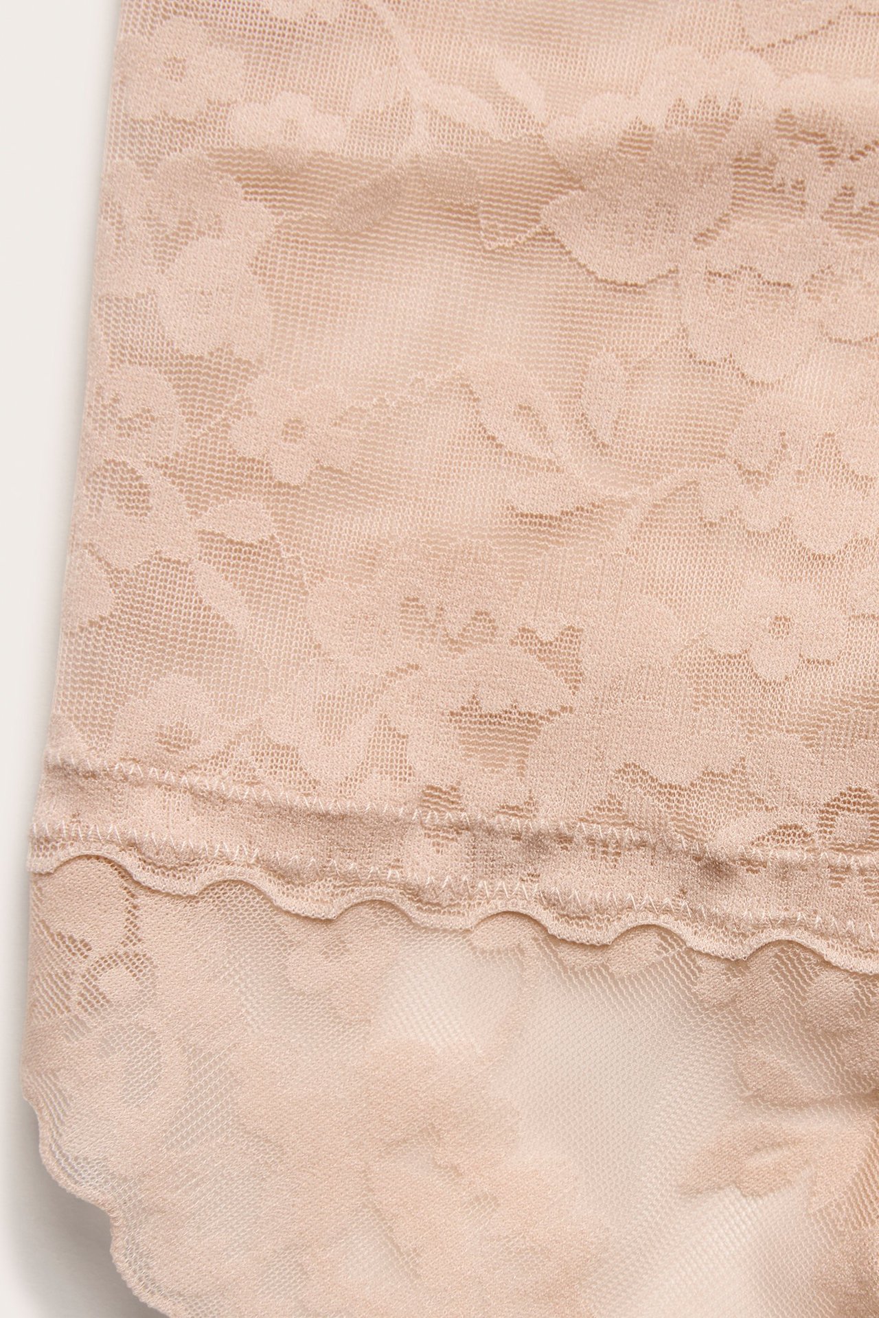 Zbliżenie jasnoróżowych koronkowych stringów modelujących z falistym brzegiem.