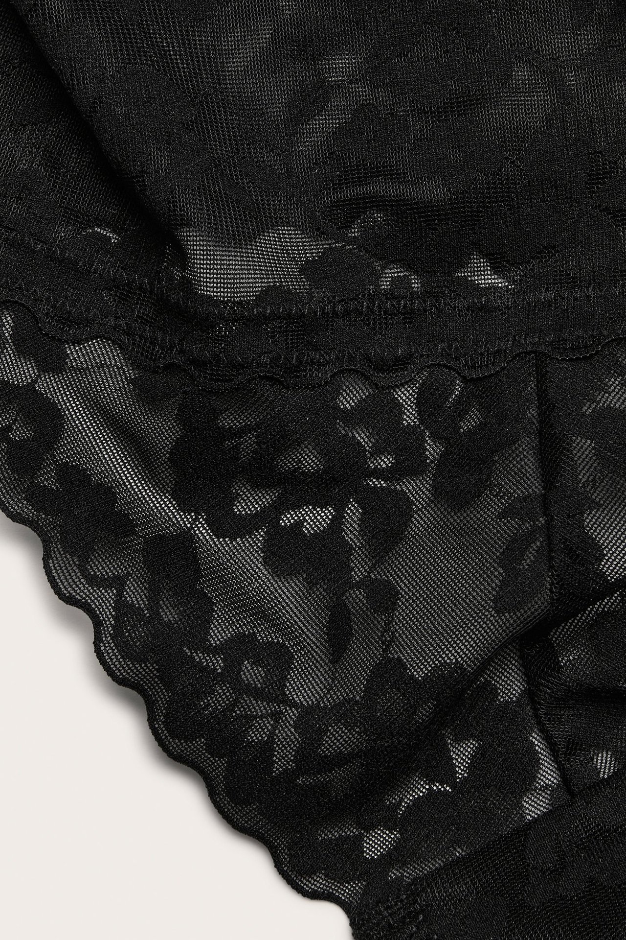 Zbliżenie na czarne koronkowe stringi z kwiatowym wzorem i falistymi brzegami.