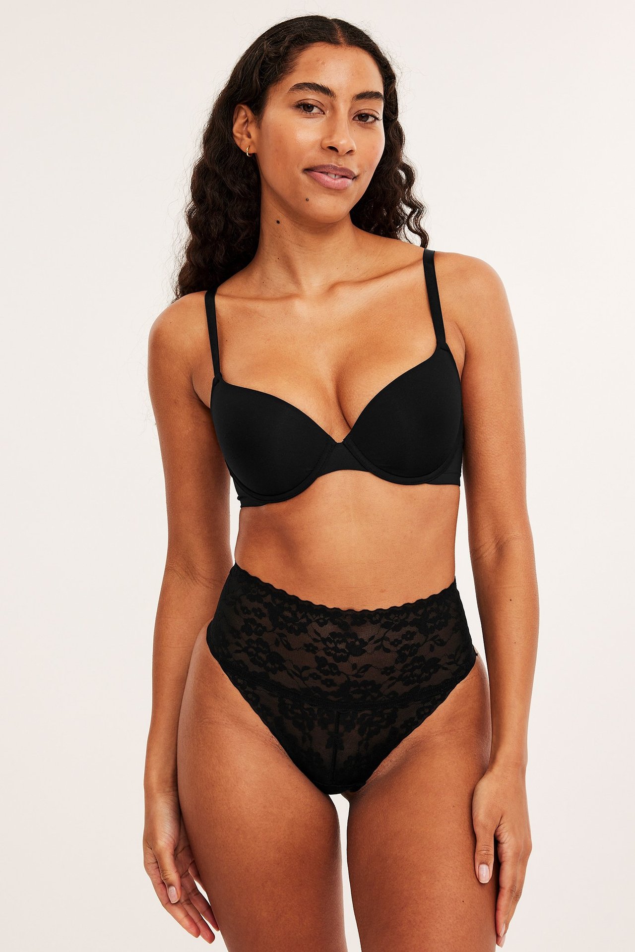 Forfra: kvinne i svart blonde-stringtruse med høy midje og shaping, samt en svart push-up-bh.