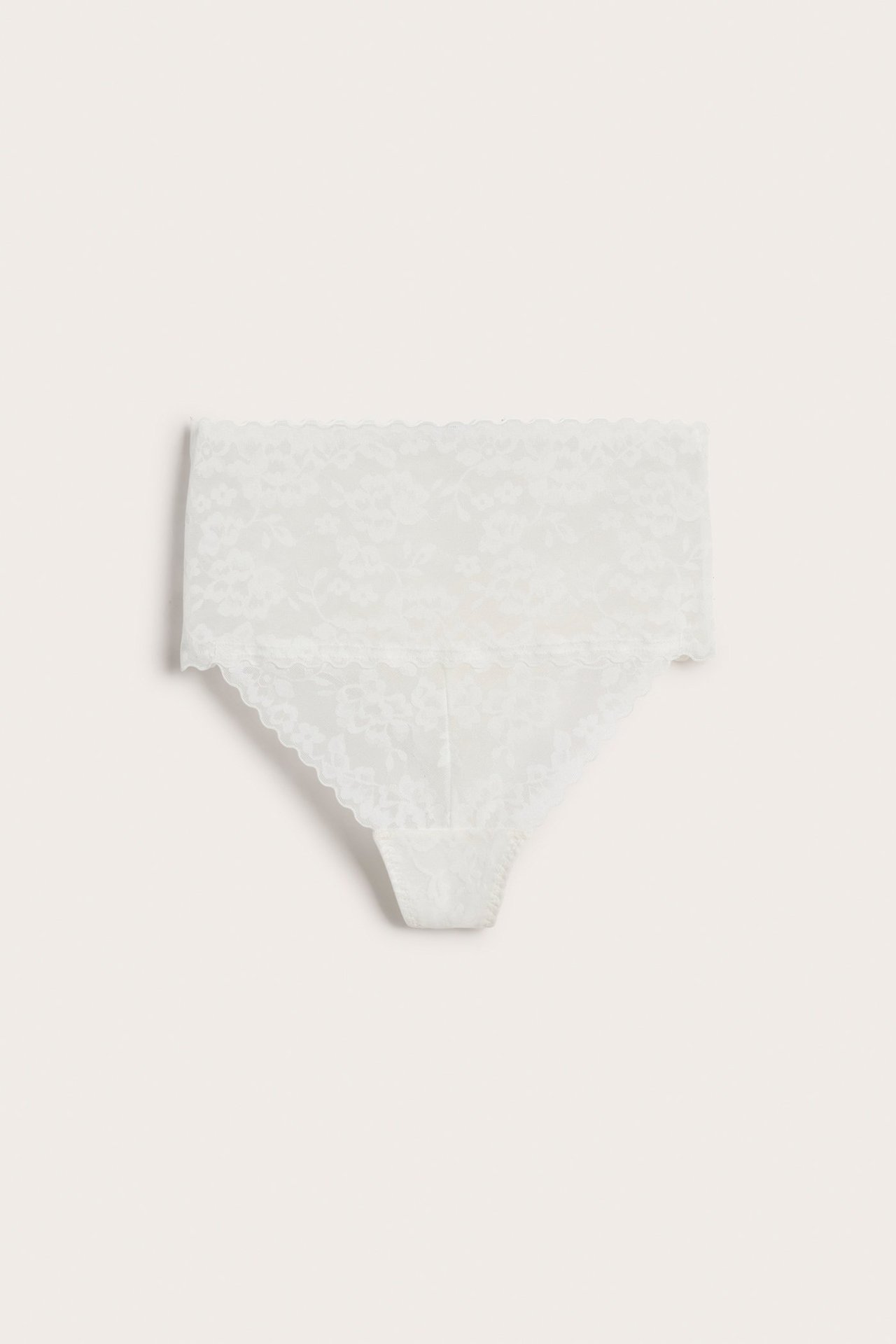 Frontvisning av en hvit høyt skåret blondestringtruse med blomstermønster.