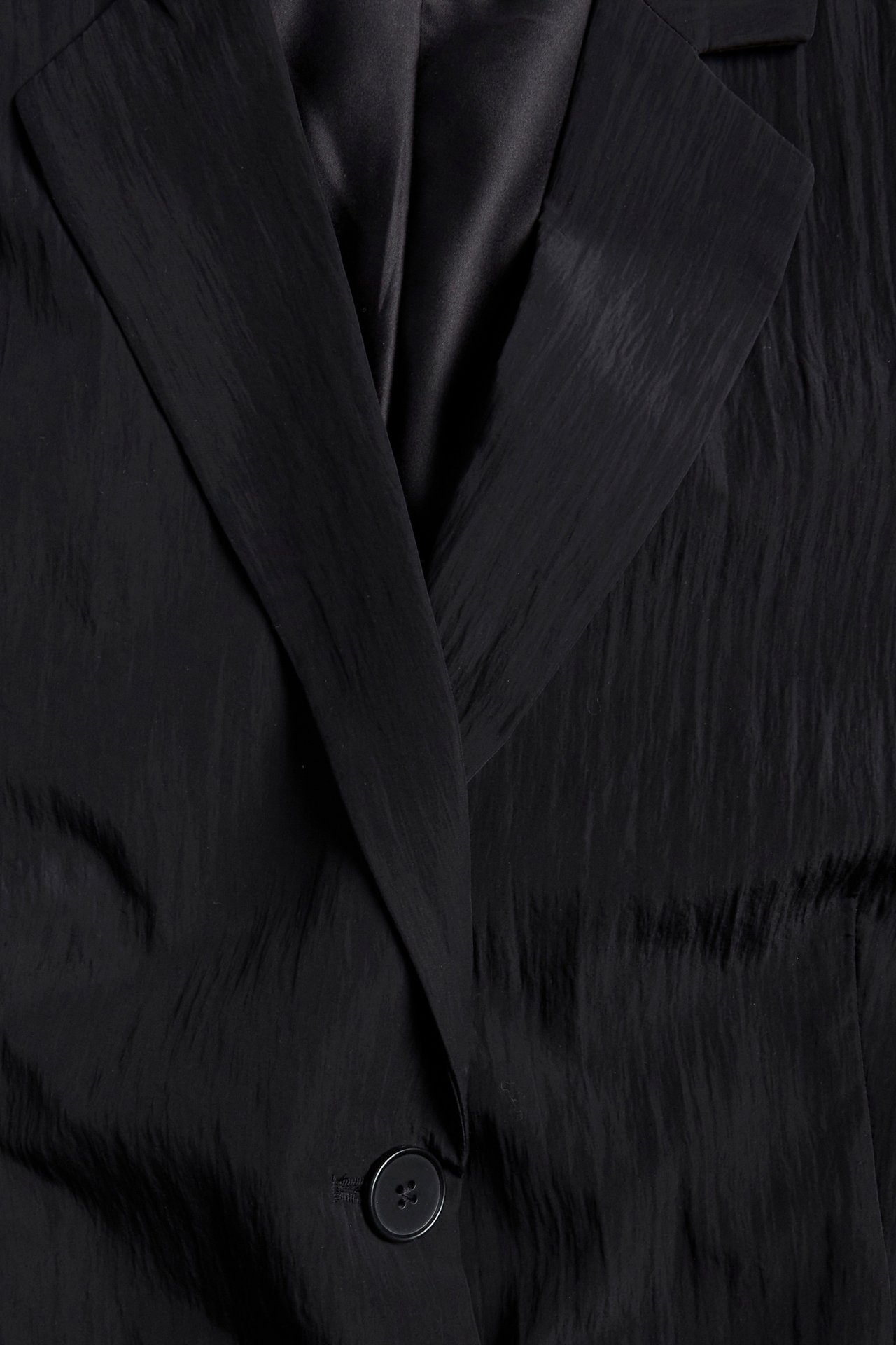 Nærbilde av en svart krøllet blazer med slag og en knapp.