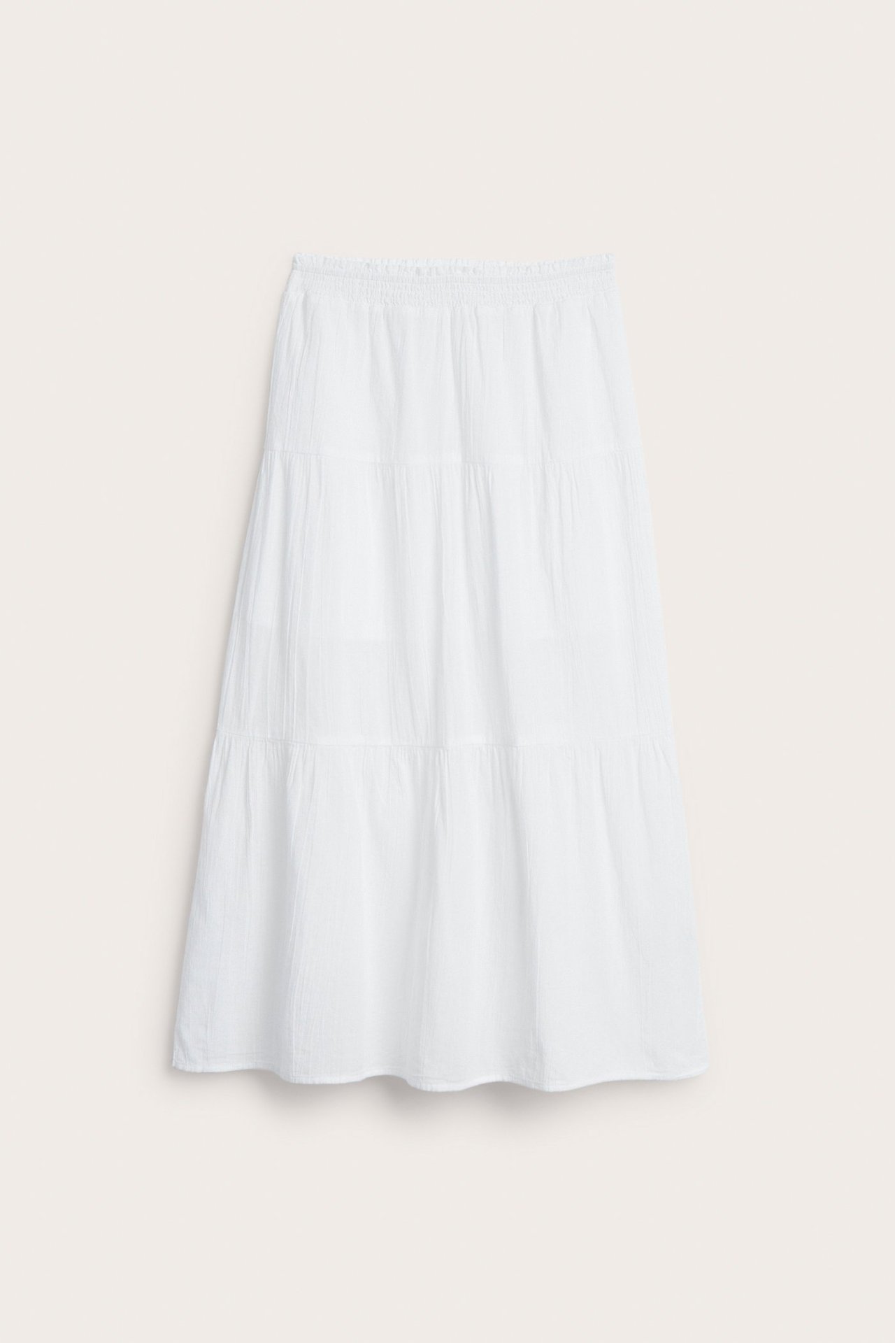 Frontvisning av et hvitt, langt skjørt i myk, vevd strukturert bomull med elastisk midje.