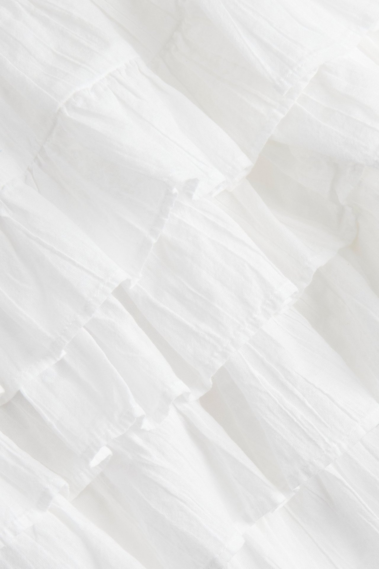 Zbliżenie białej krótkiej spódnicy z falbanami z tkanej strukturalnej bawełny.