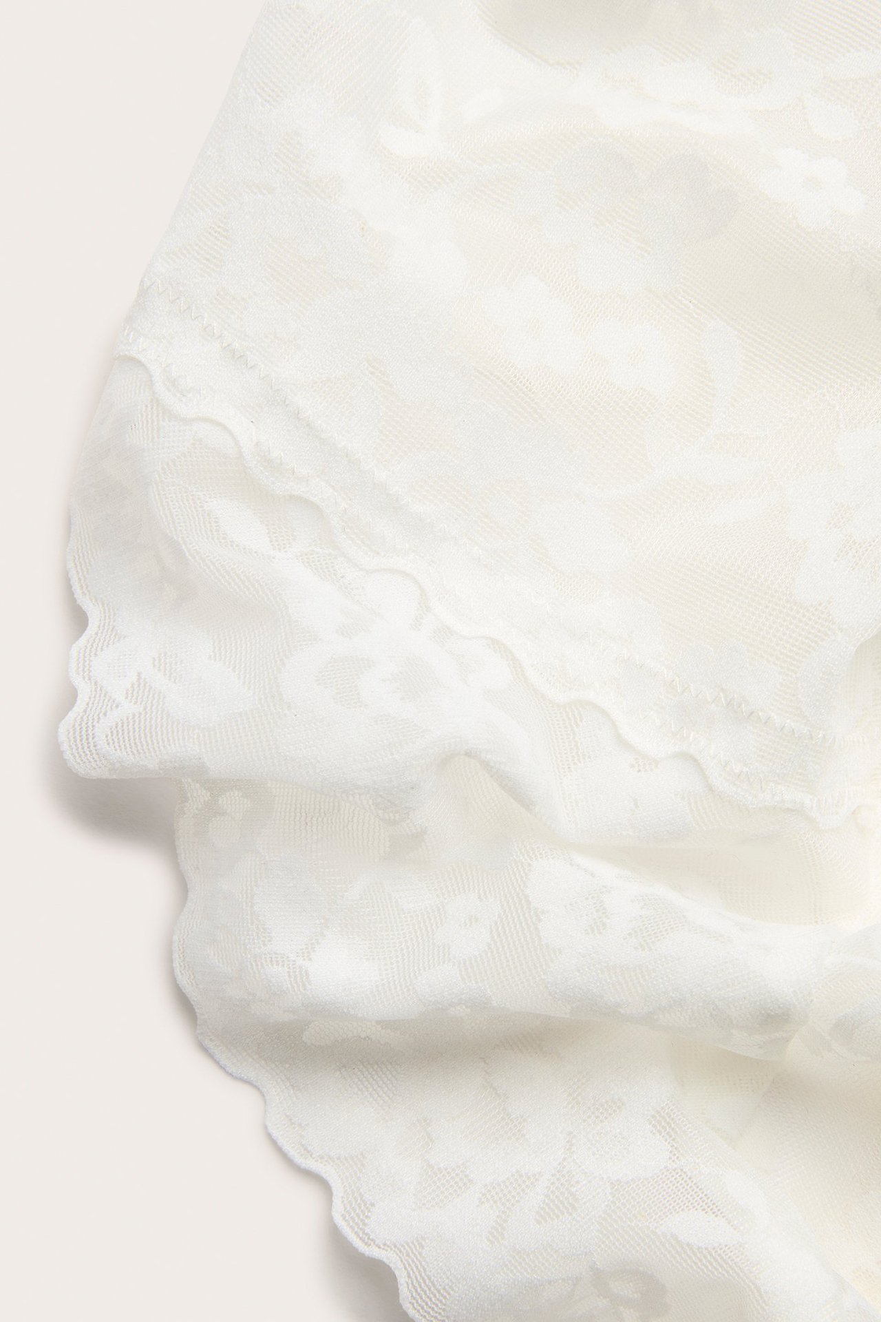 Zbliżenie białych, modelujących koronkowych fig brazilian z kwiatowym wzorem i falistym brzegiem.