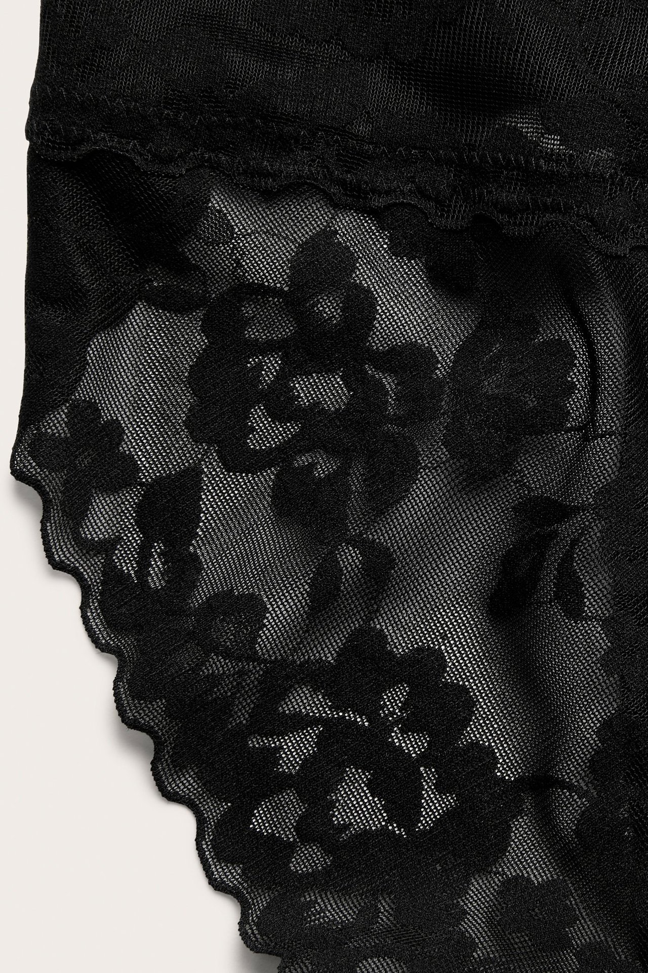 Zbliżenie czarnych koronkowych majtek modelujących brazilian z kwiatowym wzorem.