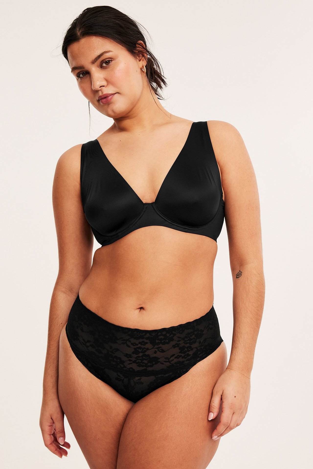 Widok z przodu kobiety w czarnych koronkowych modelujących figach brazilian i prostym czarnym biustonoszu.