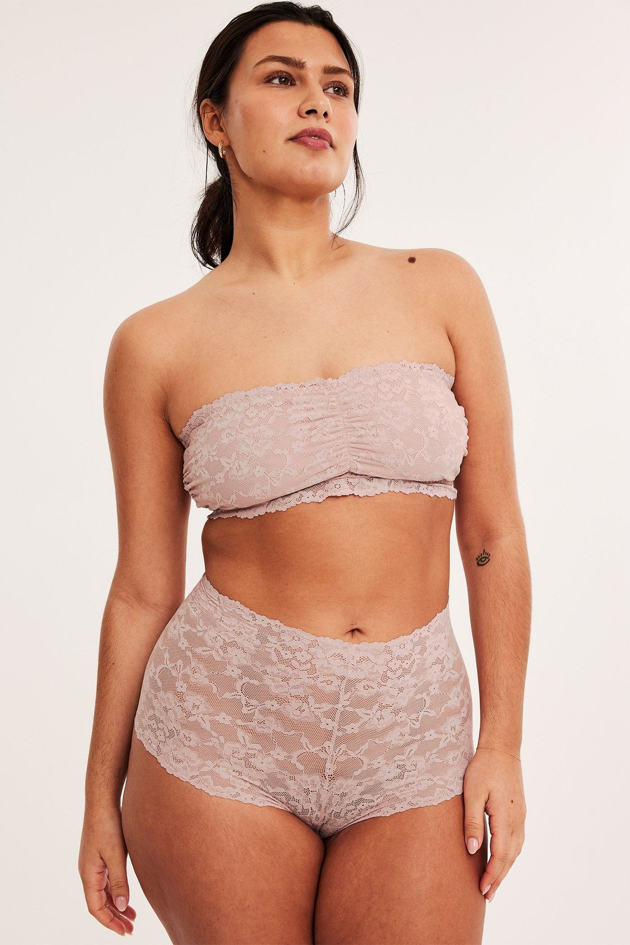 Framifrån, kvinna i ljusrosa spetsbandeau-bh och matchande spetsshorts.