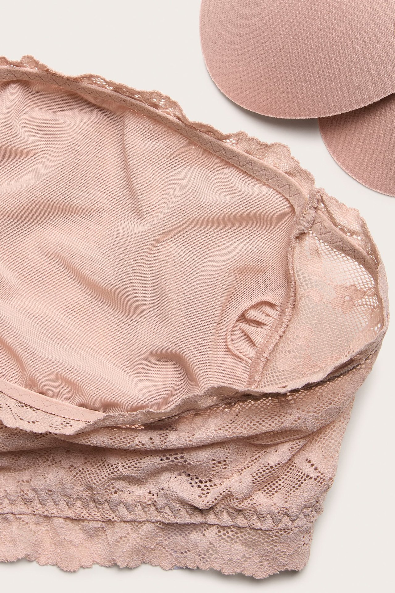 Zbliżenie jasnoróżowego koronkowego biustonosza bandeau z wyjmowanymi wkładkami obok.