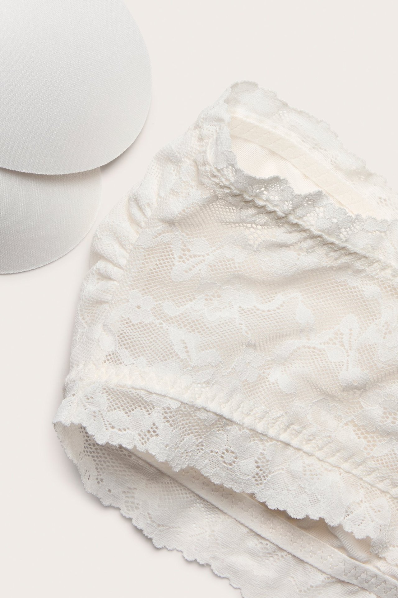 Zbliżenie na ecru koronkowy biustonosz bandeau z wyjmowanymi wkładkami.